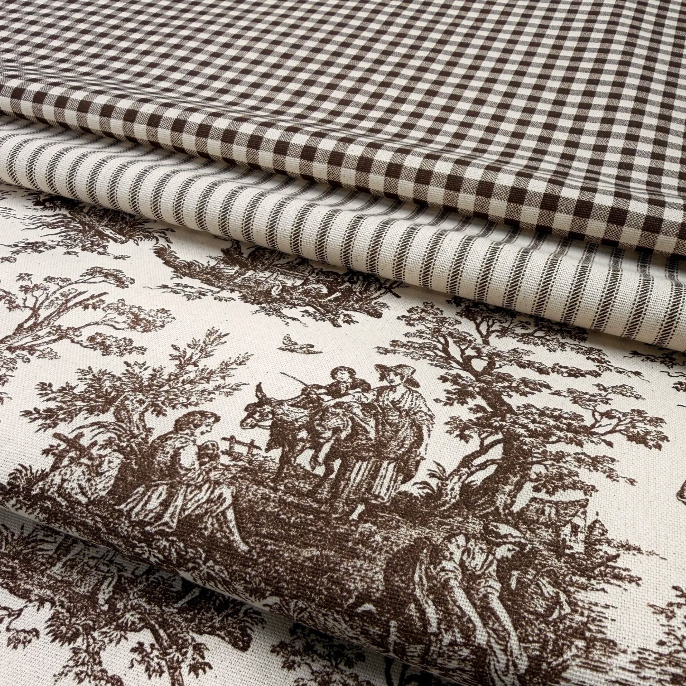 a close-up view of a fabric with a detailed brown and white pattern, including a landscape scene with people and animals. The fabric appears to be a type of quilt or textile with a checkered or gingham-like pattern.