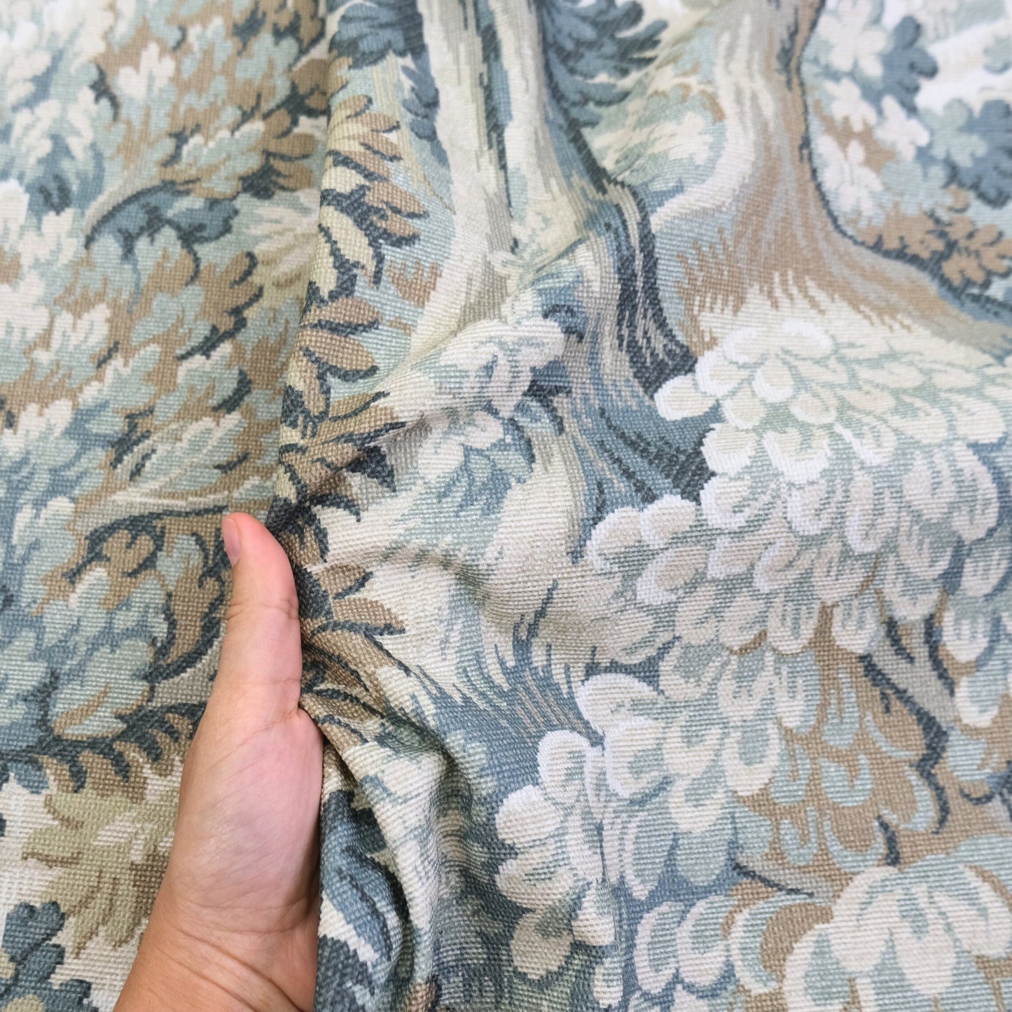A hand is holding a fabric with a floral pattern, which appears to be a close-up view of the material.