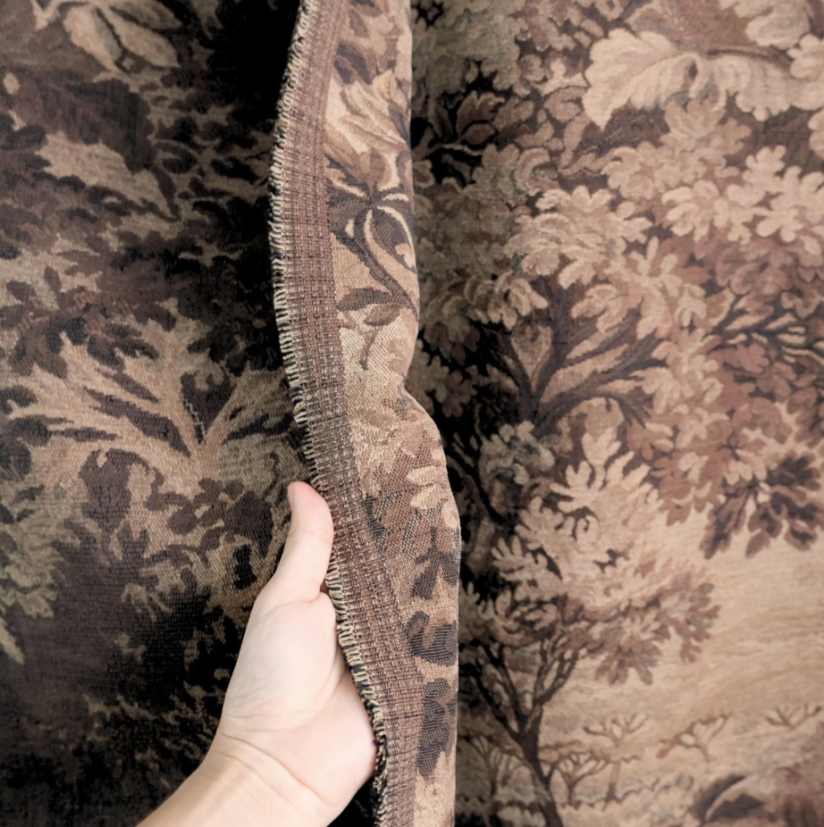 A hand is holding a piece of fabric with a floral pattern, showing the intricate details of the design.