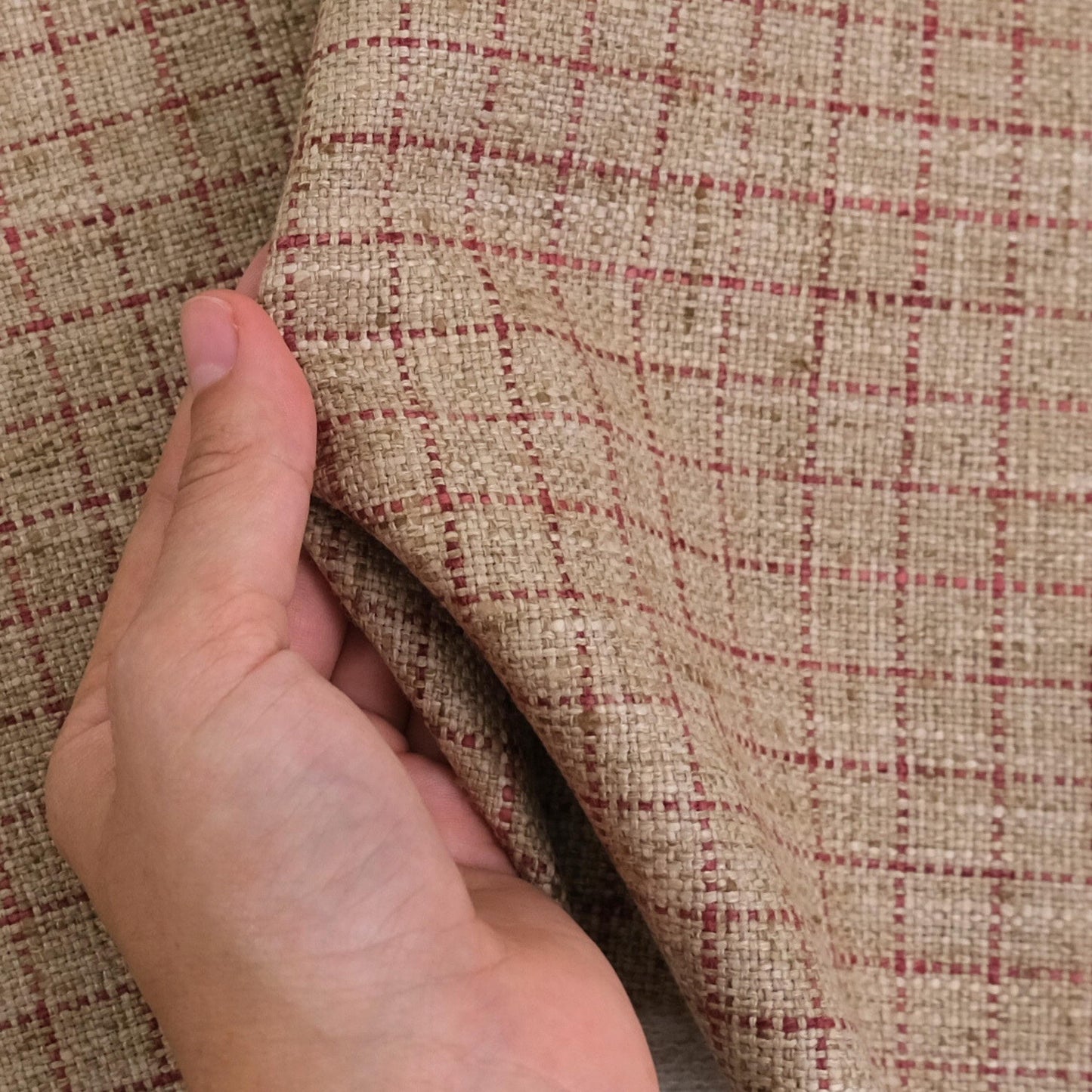 A hand is holding a fabric with a checkered pattern in red and beige colors.