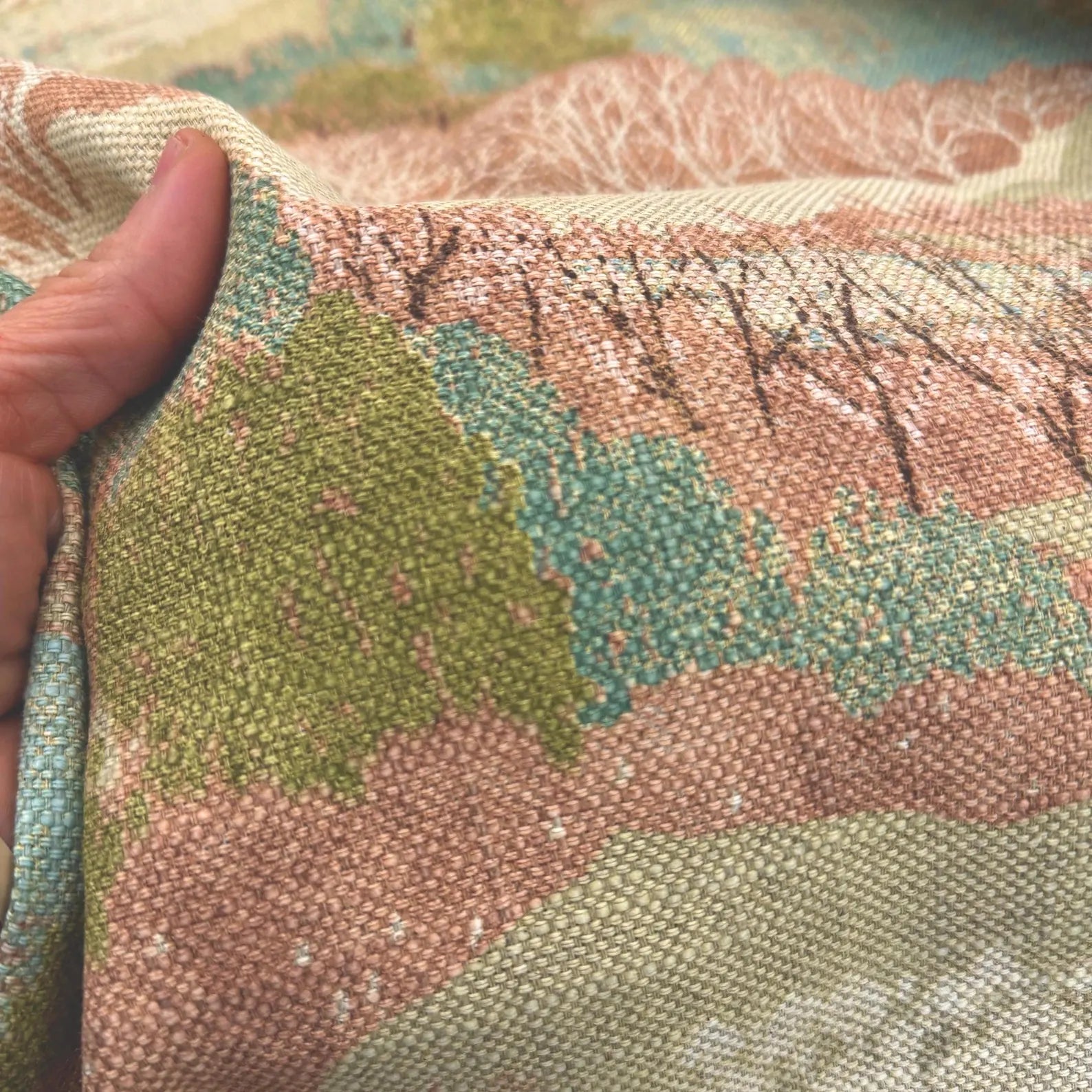 Close-up of a hand pinching the Pink Scenic Forest Fabric to showcase the 9.29 oz heavyweight cotton texture.