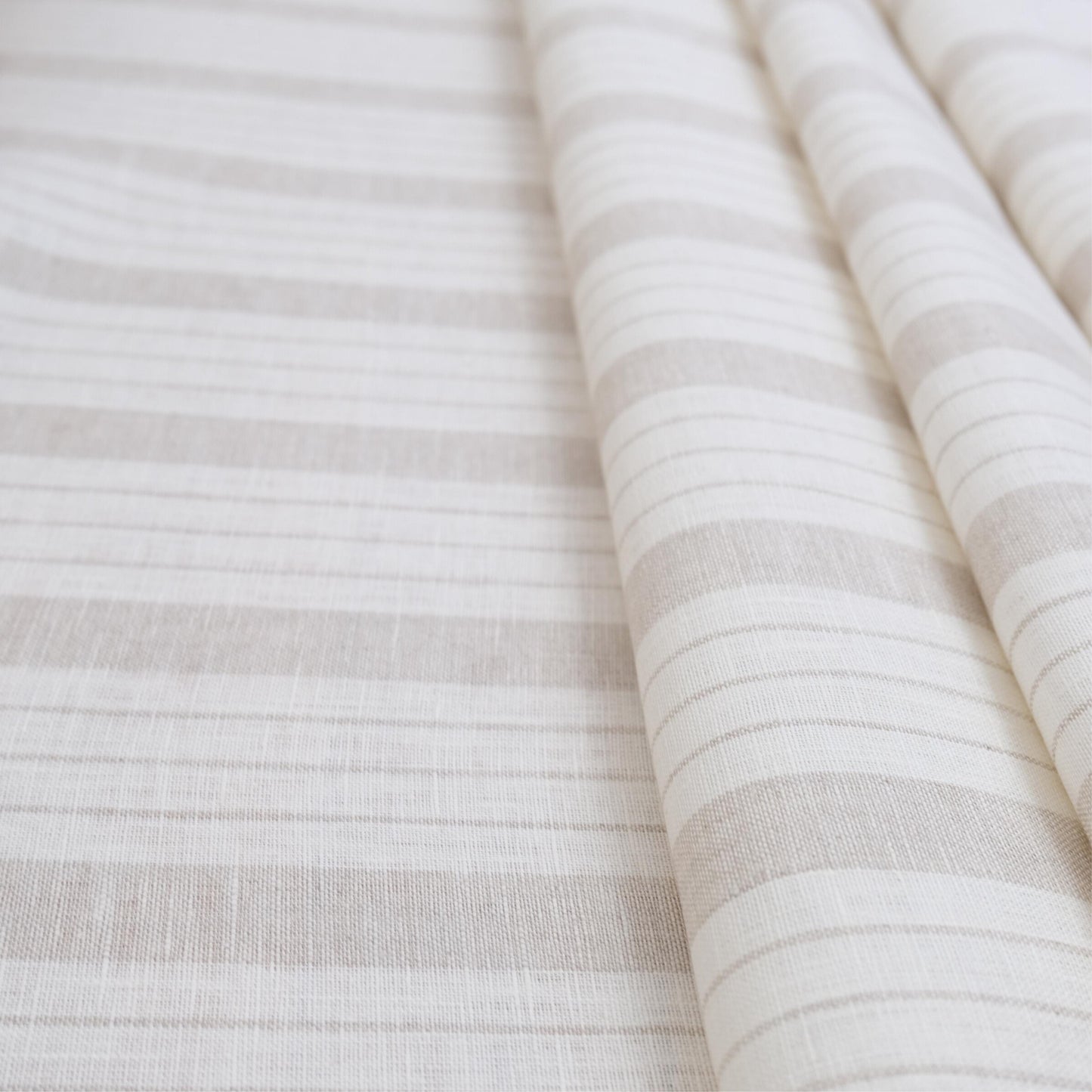 Taupe stripe linen fabric folded to showcase its soft airy weave and subtle neutral stripe design. This lightweight material is ideal for sewing curtains, table linens, pillow covers, and cottagecore-inspired home décor. Perfect for DIY sewing projects, rustic farmhouse accents, neutral minimalist interiors, and versatile décor crafts where natural linen texture adds charm and durability.
