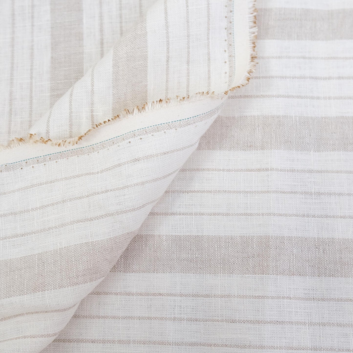 Taupe stripe linen fabric styled in folds, showing airy drape, breathable weave, and soft neutral tones. This striped fabric is ideal for farmhouse table décor, minimalist curtains, cottage-inspired napkins, and rustic DIY home projects. The natural linen texture and classic stripe design make it a versatile material for sewing projects that require elegance and durability, such as lightweight drapery, tablecloths, or soft furnishings.