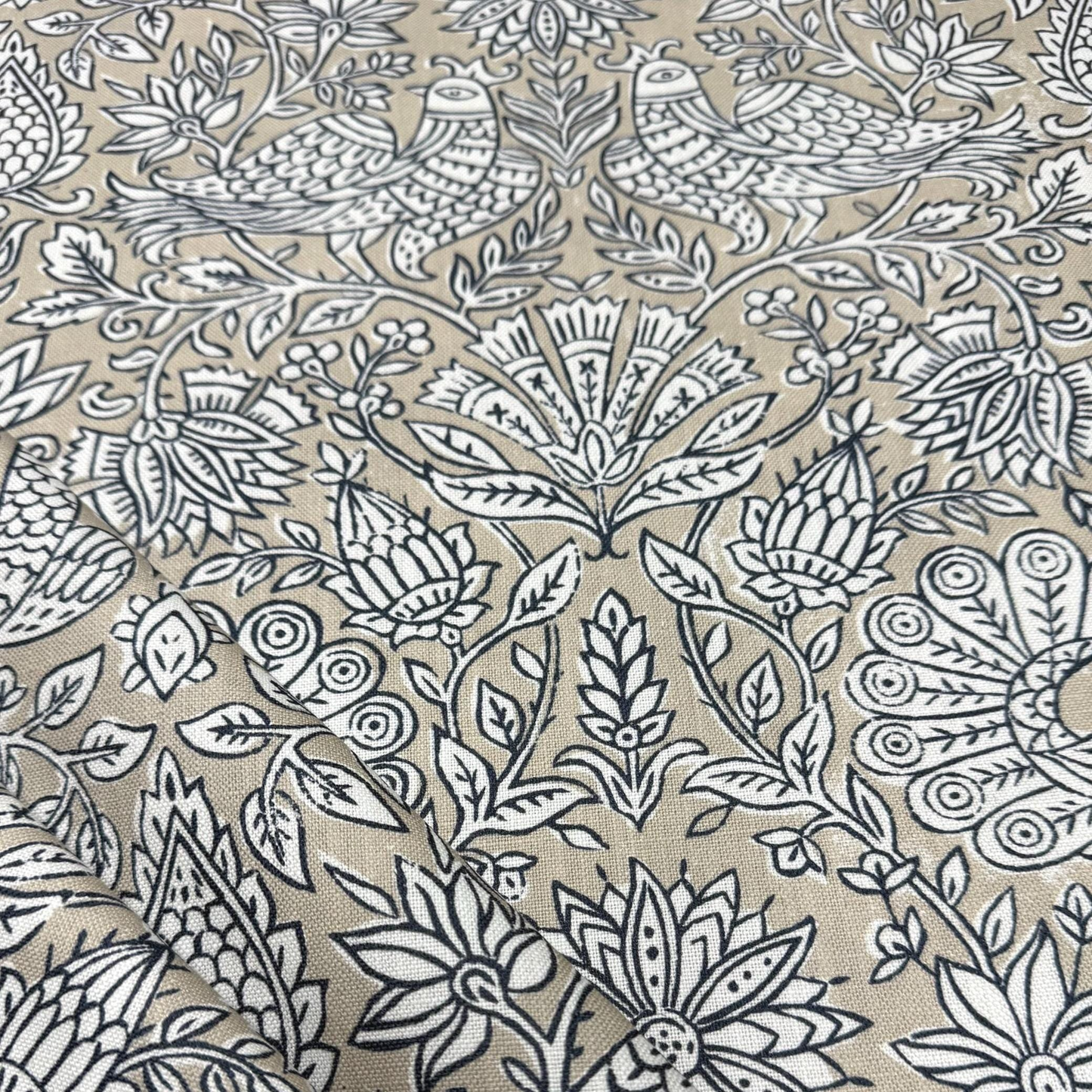 a close-up view of a fabric with a repeating floral pattern in shades of beige and black. The pattern consists of various flowers and leaves, creating a visually striking and intricate design. The image does not contain any text or other discernible objects or actions.