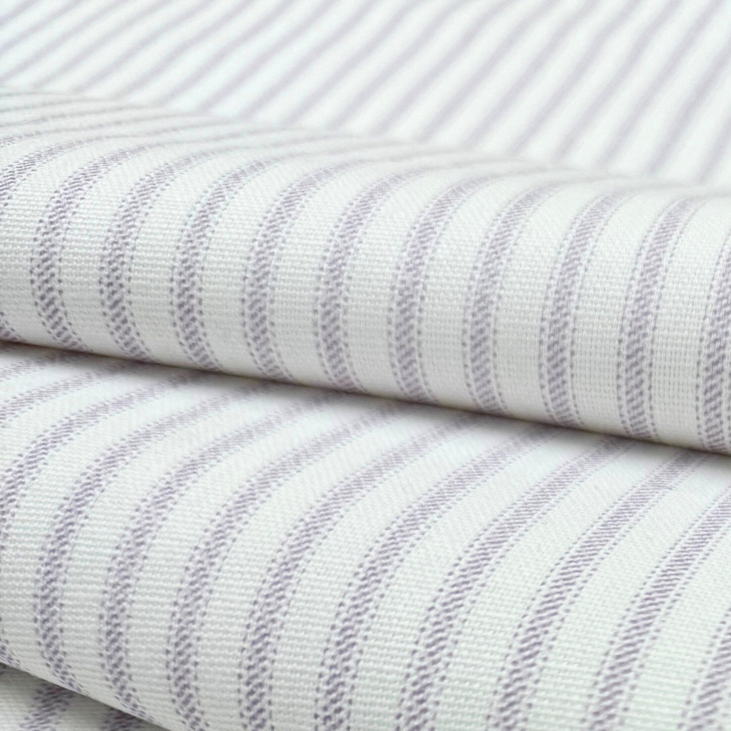 a close-up view of a fabric with a striped pattern in shades of white and purple. The fabric appears to be folded or rolled, with the edges of the fabric visible.