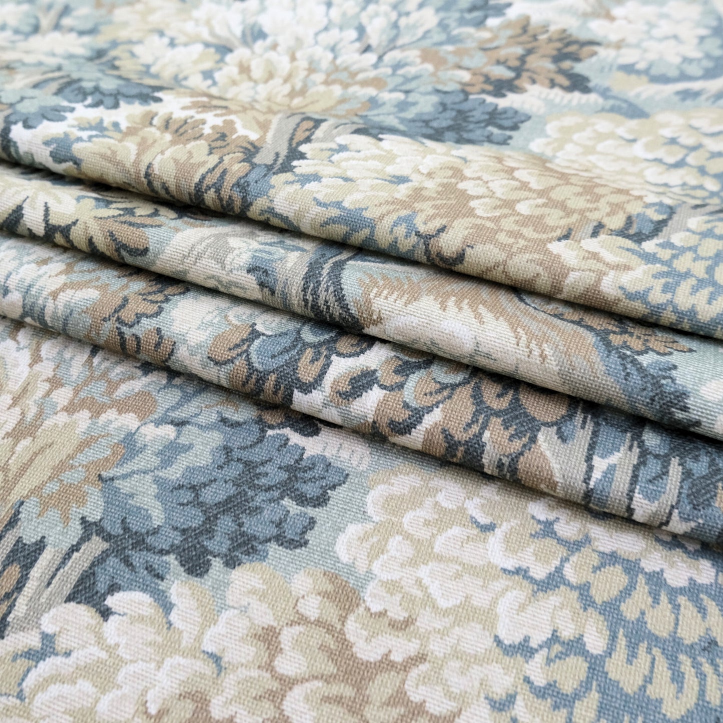 a close-up view of a fabric with a floral pattern in shades of blue, green, and beige. The fabric appears to be folded or rolled, revealing the intricate design and texture of the material.