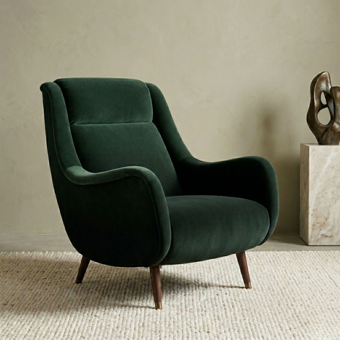 A dark green armchair with a curved backrest and armrests sits against a beige wall, accompanied by a sculpture on a pedestal.