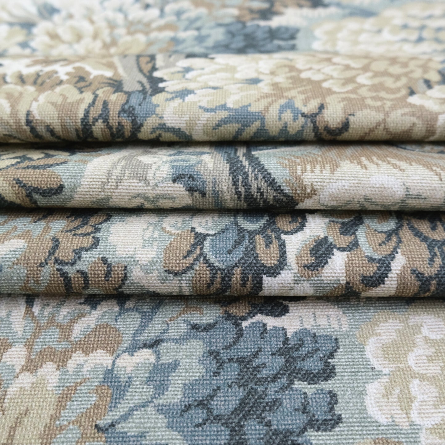 a close-up view of a fabric with a floral pattern in shades of blue, green, and beige. The fabric appears to be folded or rolled, revealing the intricate design and texture of the material.