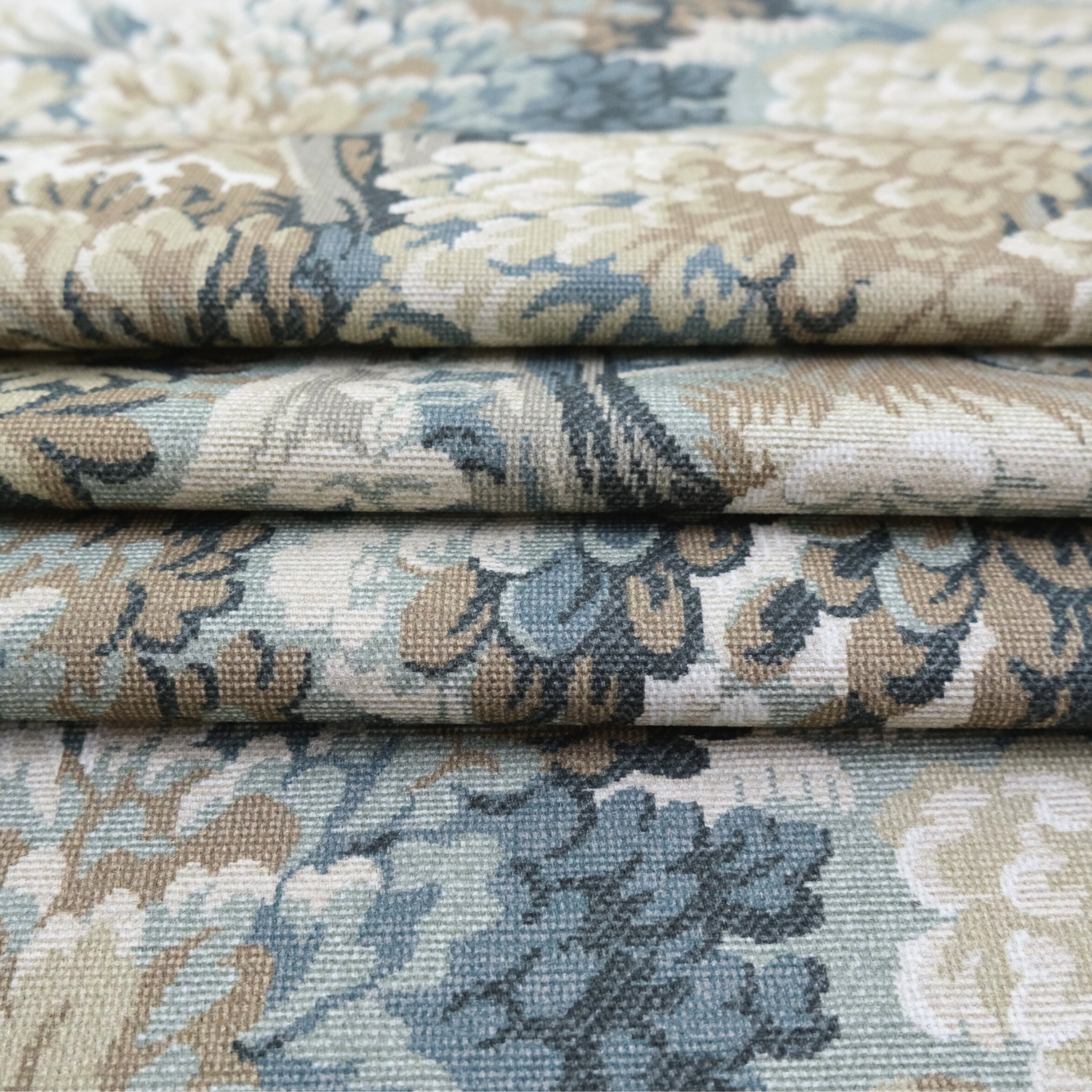 a close-up view of a fabric with a floral pattern in shades of blue, green, and beige. The fabric appears to be folded or rolled, revealing the intricate design and texture of the material.