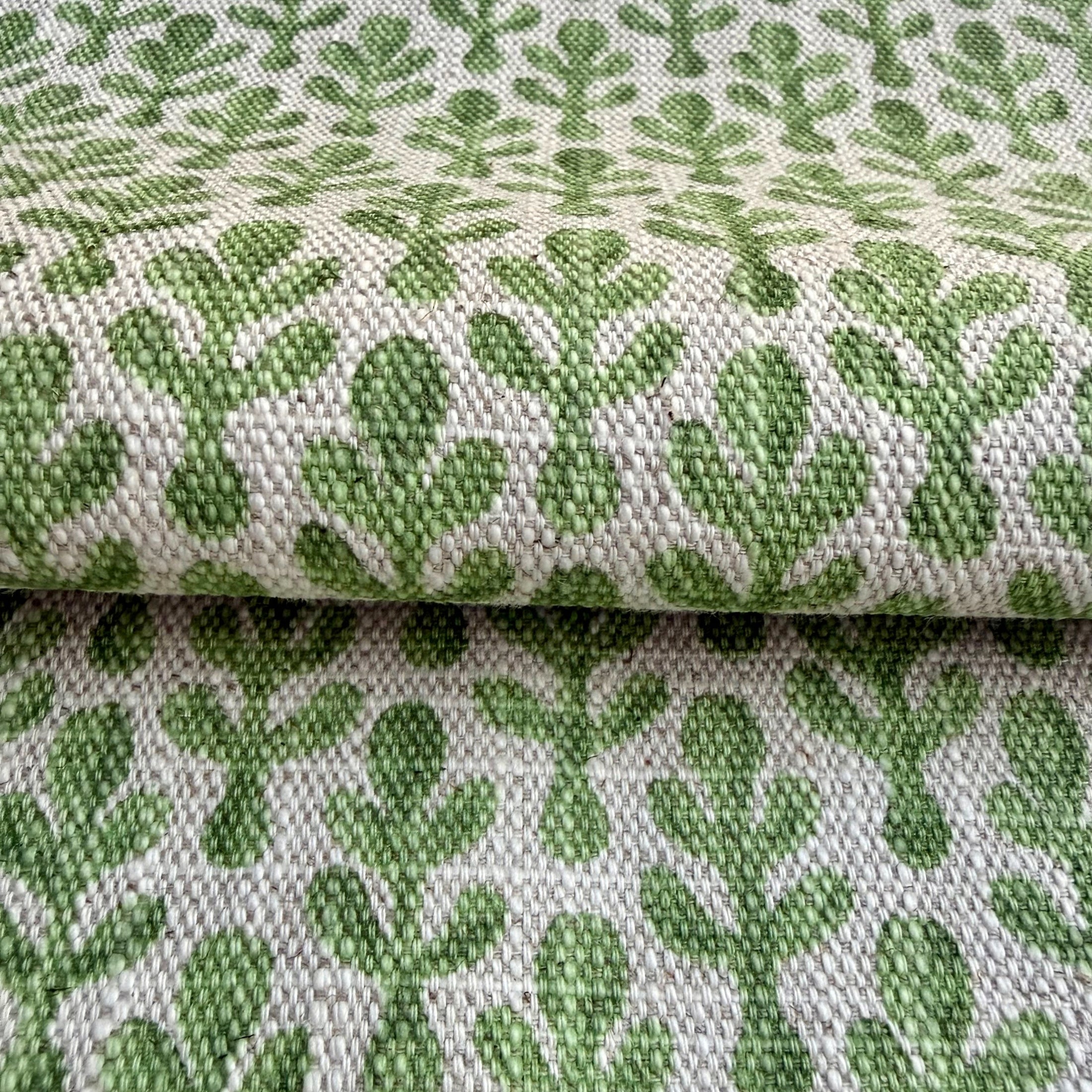 a close-up view of a fabric with a repeating pattern of green cactus leaves. The pattern is woven into the fabric, creating a textured and visually appealing design.