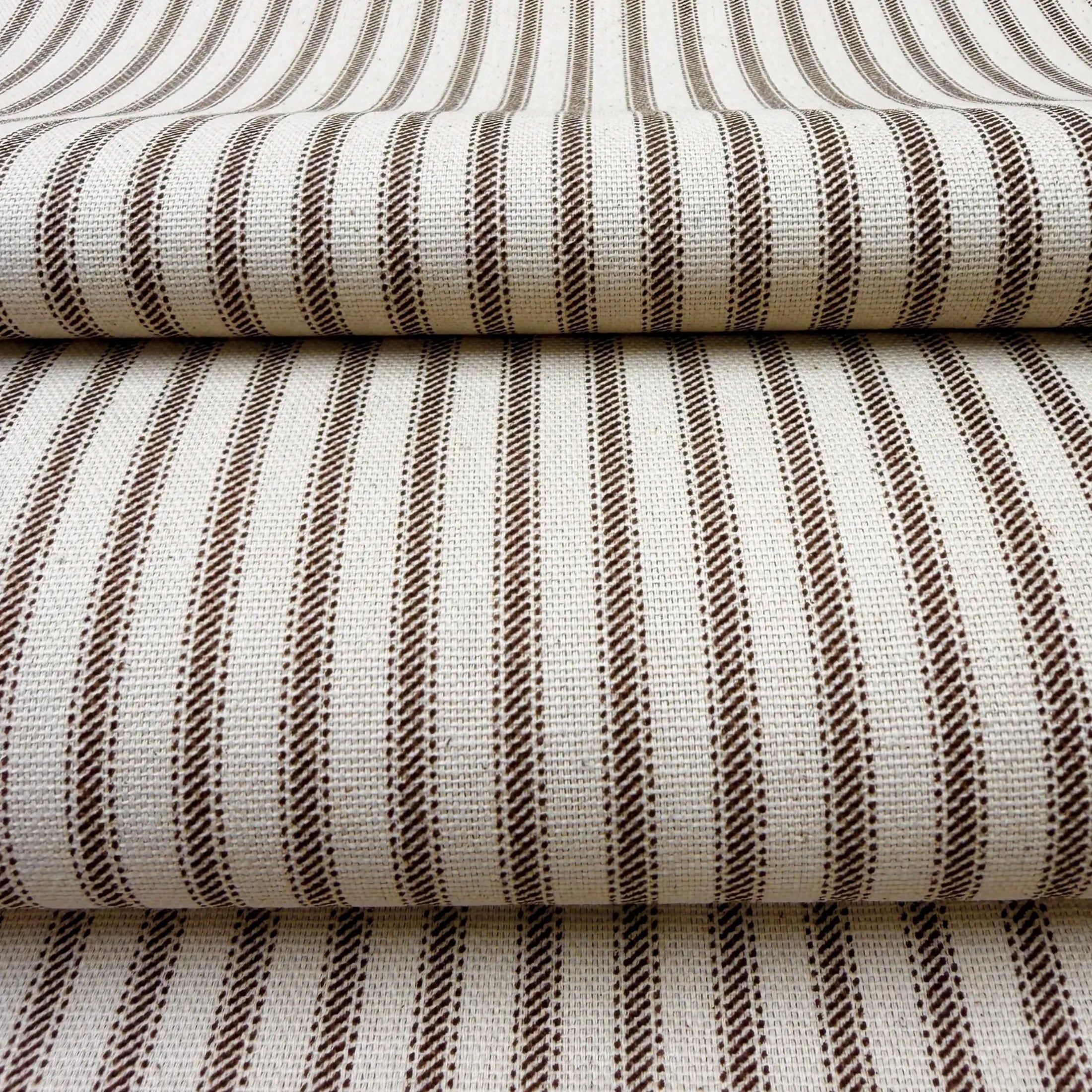 a close-up view of a fabric with a striped pattern in shades of brown and white. The fabric appears to be folded or stacked, creating a layered effect.