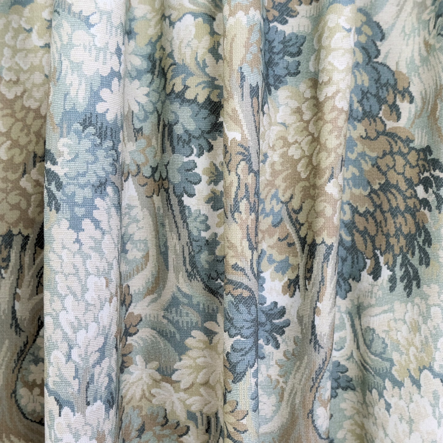 a close-up view of a fabric with a floral pattern in shades of blue, green, and beige. The fabric appears to be made of a woven material, with a textured and intricate design.