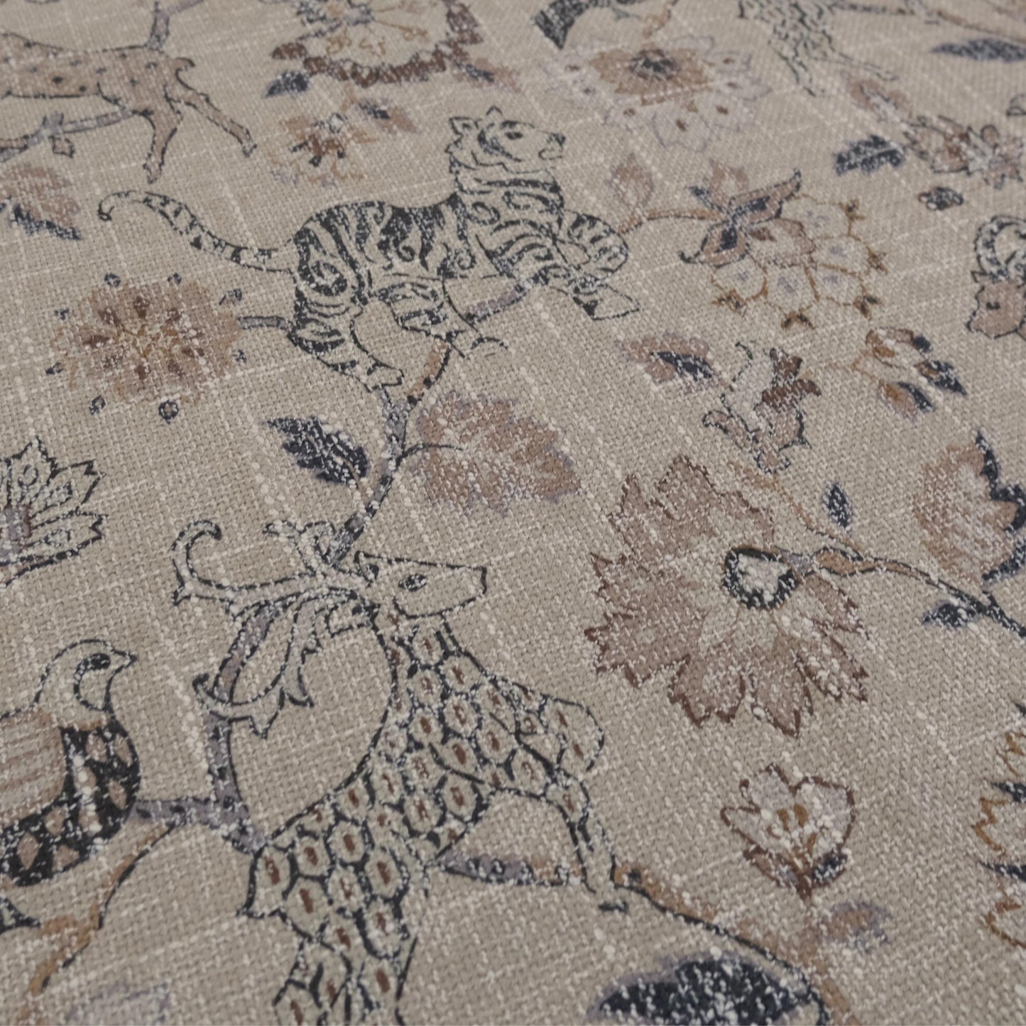Beige fabric with a repeating pattern of stylized animals and floral elements. The design features tigers, deer, and birds interspersed with large, ornate flowers and foliage in shades of brown and gray. The fabric has a textured appearance.