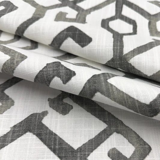a close-up view of a fabric with a repeating geometric pattern in shades of gray and white. The pattern consists of various shapes and lines, creating a visually striking and intricate design.
