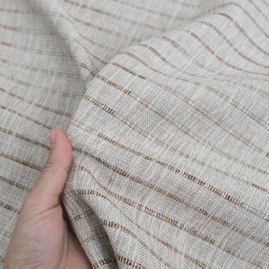 A close-up view of a hand holding a fabric with a striped pattern in shades of beige and brown.