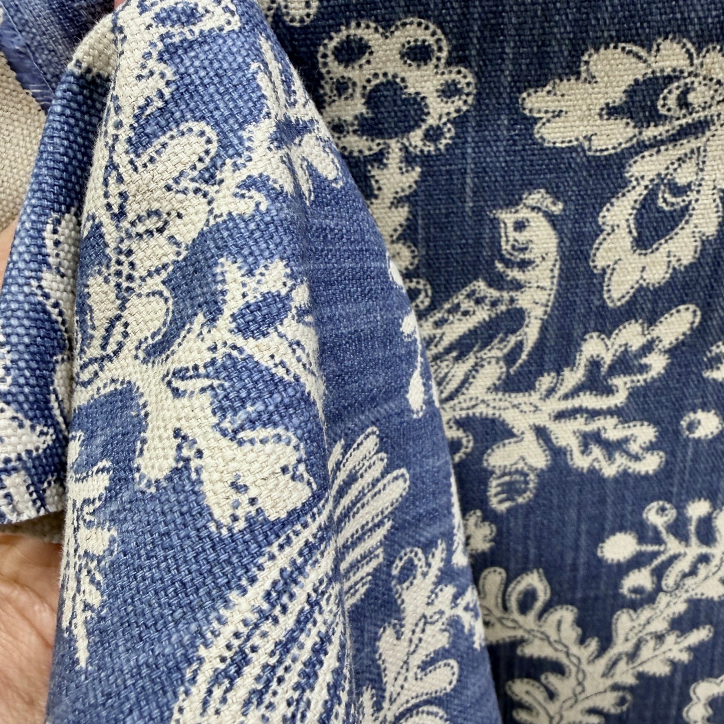Blue and cream floral upholstery fabric held to show thickness, texture, and drape