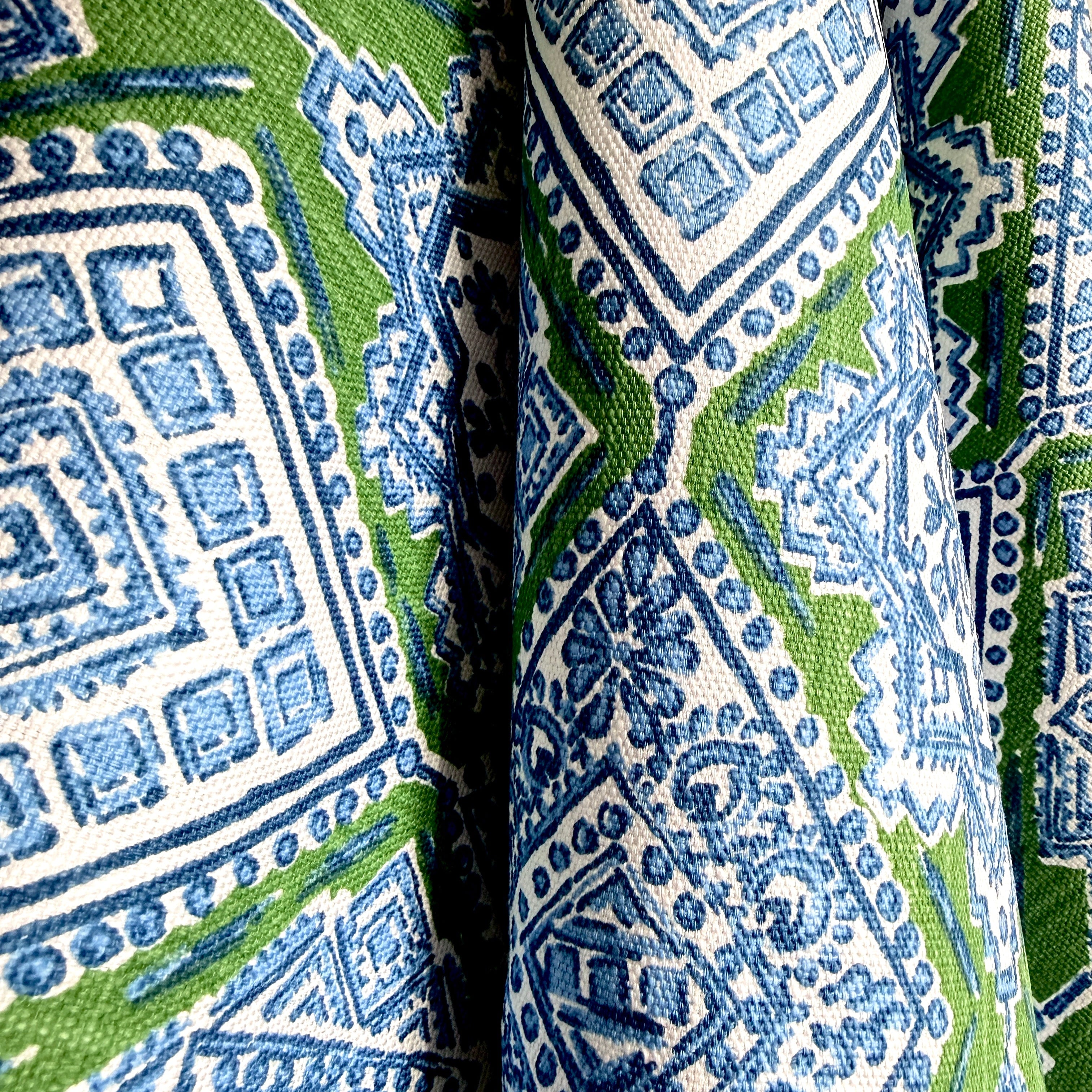 A close-up of patterned fabric with an intricate geometric moroccan tile pattern print in blue and green on a white background.