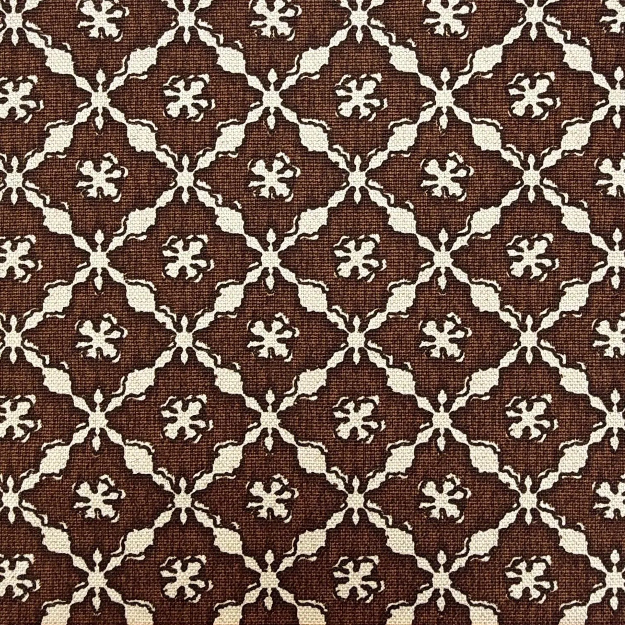 a close-up view of a fabric with a repeating pattern of brown and white flowers or designs. The pattern is intricate and detailed, with the flowers or designs appearing in various sizes and orientations. The fabric appears to be made of a woven material, and there is a ruler placed at the bottom of the image for scale.