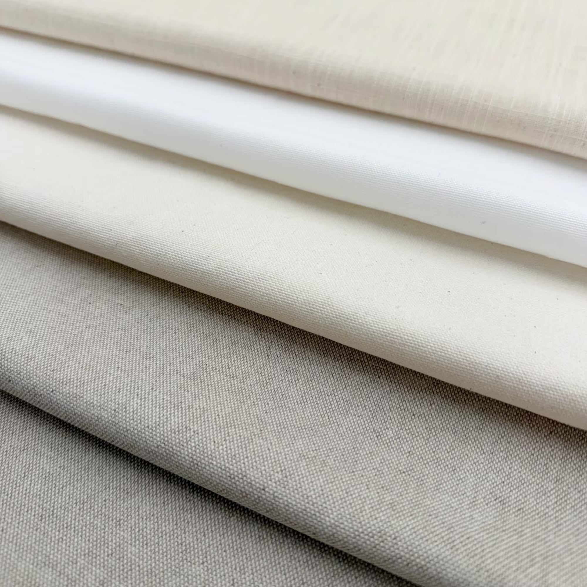 A close-up image of various fabric swatches in shades of white, gray, and beige, arranged in a layered fashion.