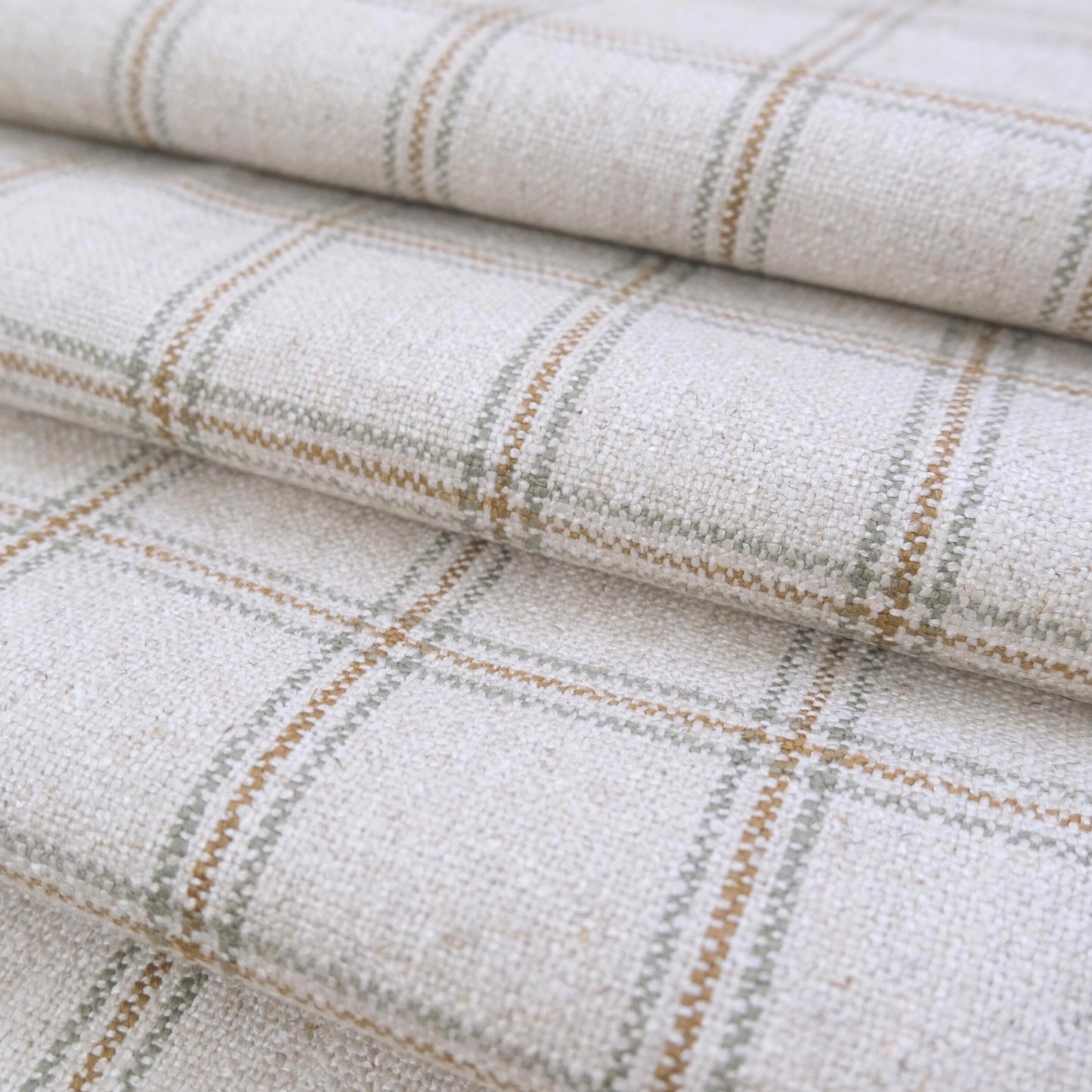 May include: Close-up of a woven fabric with a plaid pattern. The fabric is primarily off-white with intersecting lines in shades of brown and gray, creating a grid-like design. The texture appears slightly uneven, suggesting a natural fiber material.