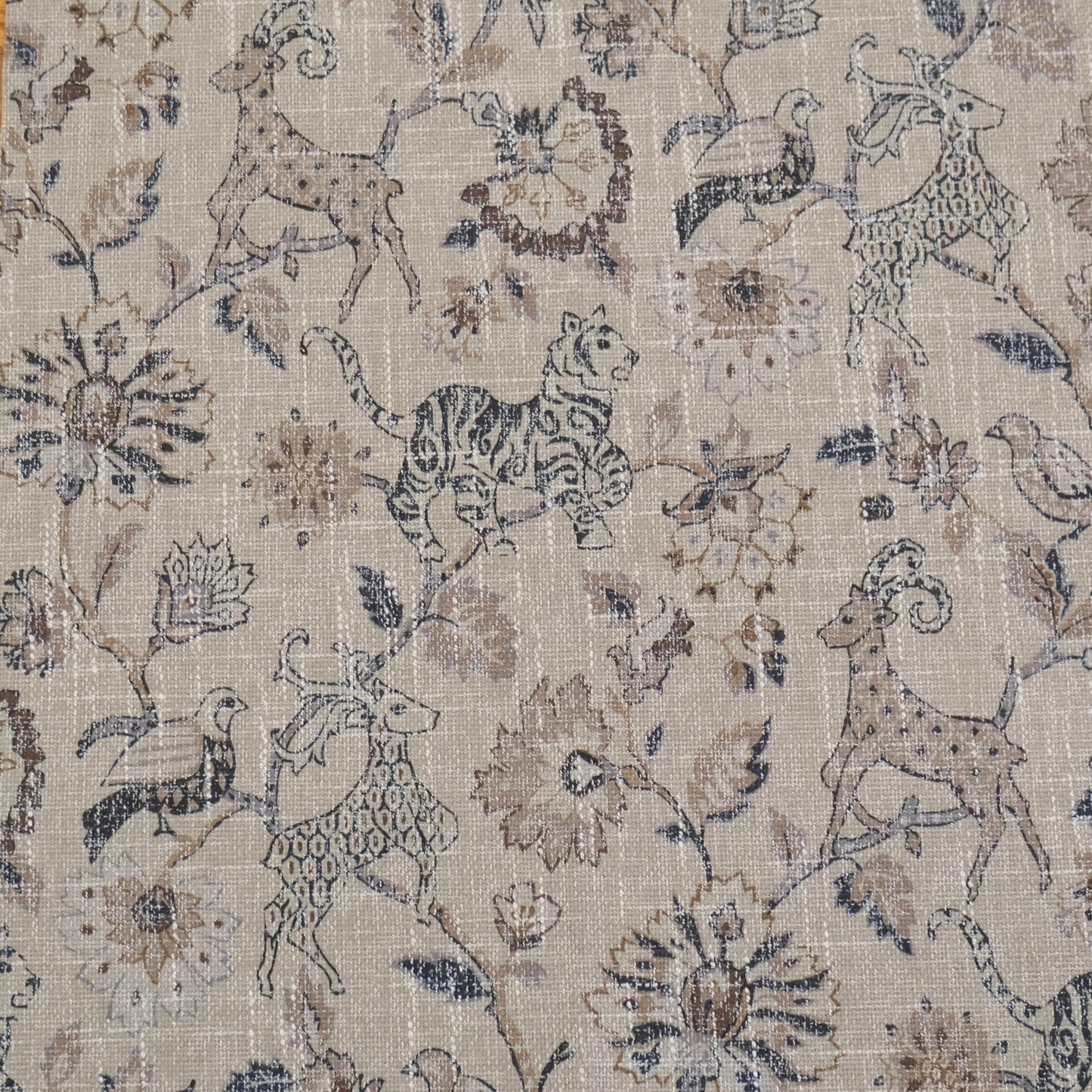 Beige fabric with a repeating pattern of stylized animals and floral elements. The design features a deer, tiger, and birds among ornate flowers and foliage. The color palette includes shades of brown, beige, and hints of green, creating a vintage, textured look.