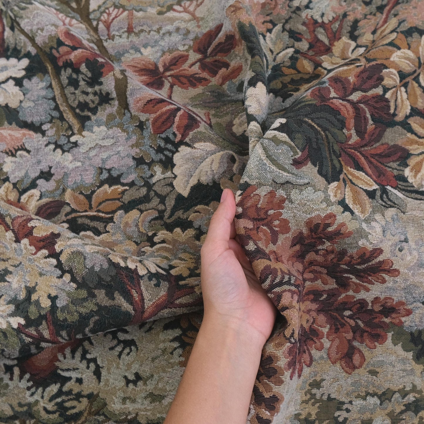 Hand holding heavyweight tapestry upholstery fabric in Woodrose foliage pattern, woven jacquard textile with scenic verdure design, antique style upholstery material perfect for sofas, armchairs, ottomans, curtains, wall hangings, and furniture restoration projects.