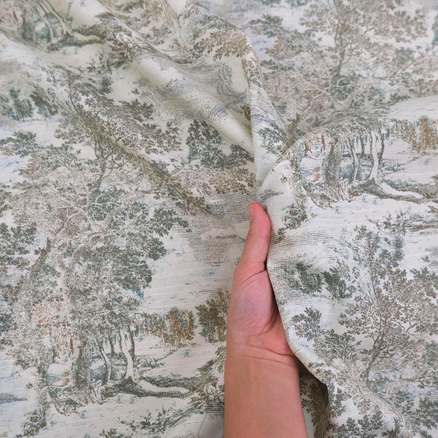 A hand is holding a fabric with a pattern of trees and foliage, suggesting it is a piece of clothing or textile with a nature-inspired design.