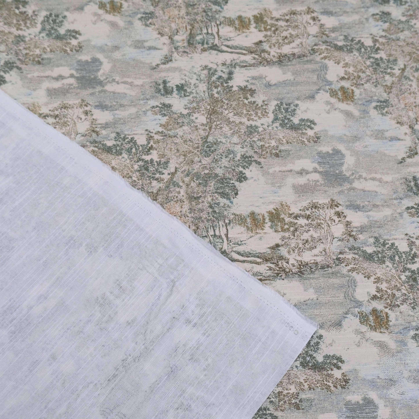 a close-up view of a fabric with a pattern of trees and foliage, including a landscape scene. The fabric appears to be a piece of cloth or textile, with a white or light-colored background. The pattern on the fabric is intricate and detailed, showcasing the craftsmanship and design elements.