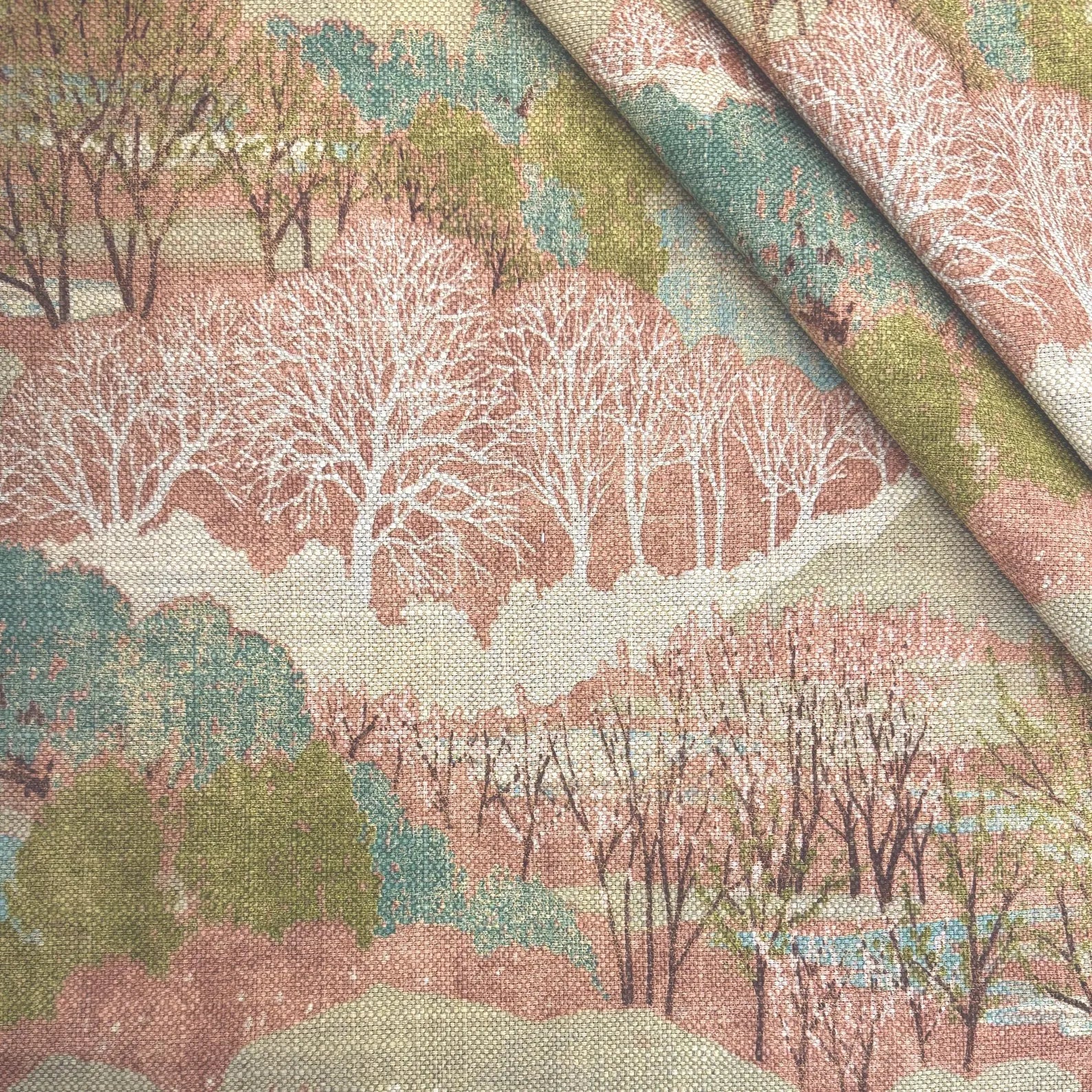 The Pink Scenic Forest Landscape Fabric folded diagonally, demonstrating its textile weight, woven texture, and suitability for upholstery and drapery.