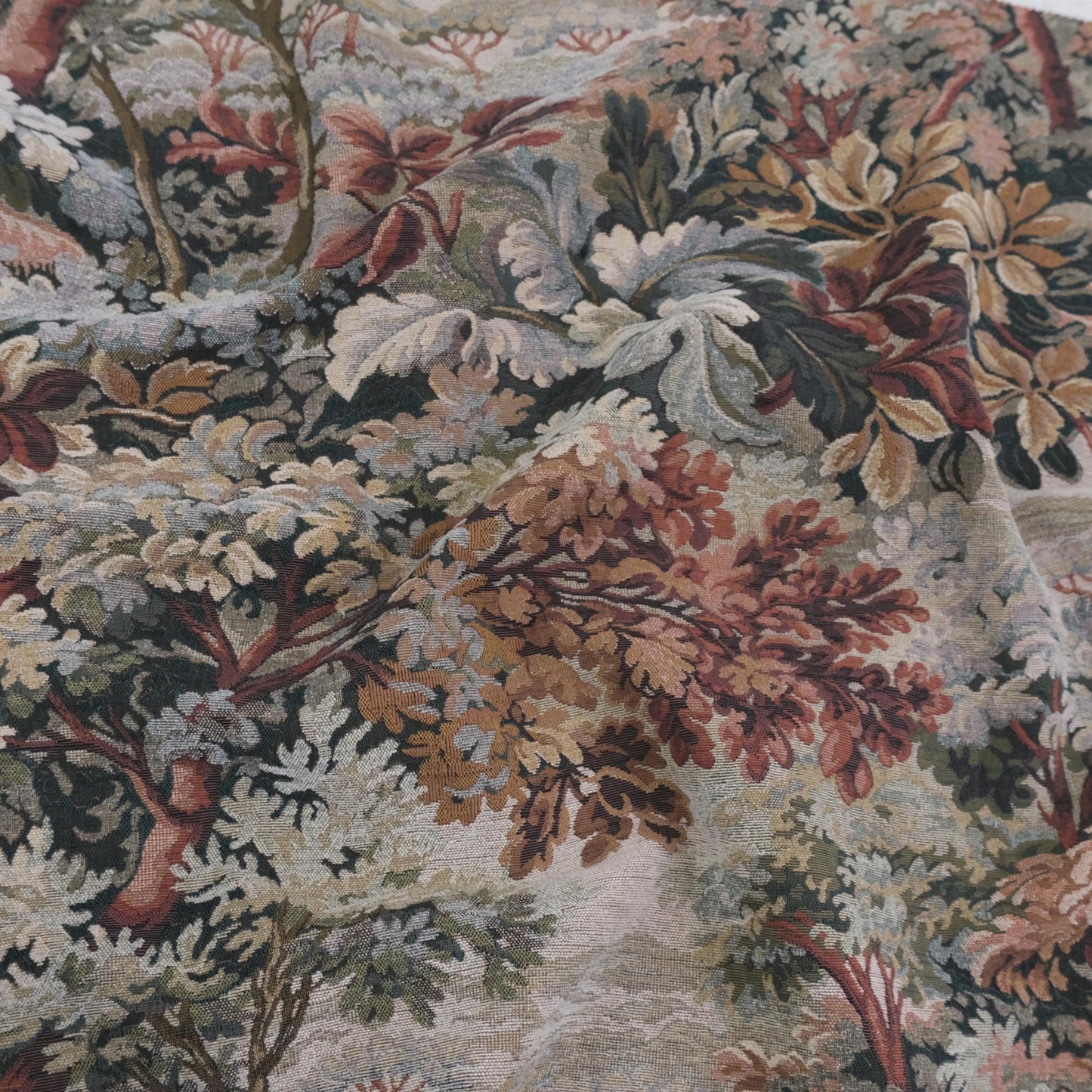 Scenic foliage tapestry upholstery fabric in warm Woodrose tones draped across surface, heavyweight jacquard textile with verdure design, antique style woven fabric by the yard for drapery, slipcovers, vintage furniture upholstery, decorative pillows, and wall hangings.