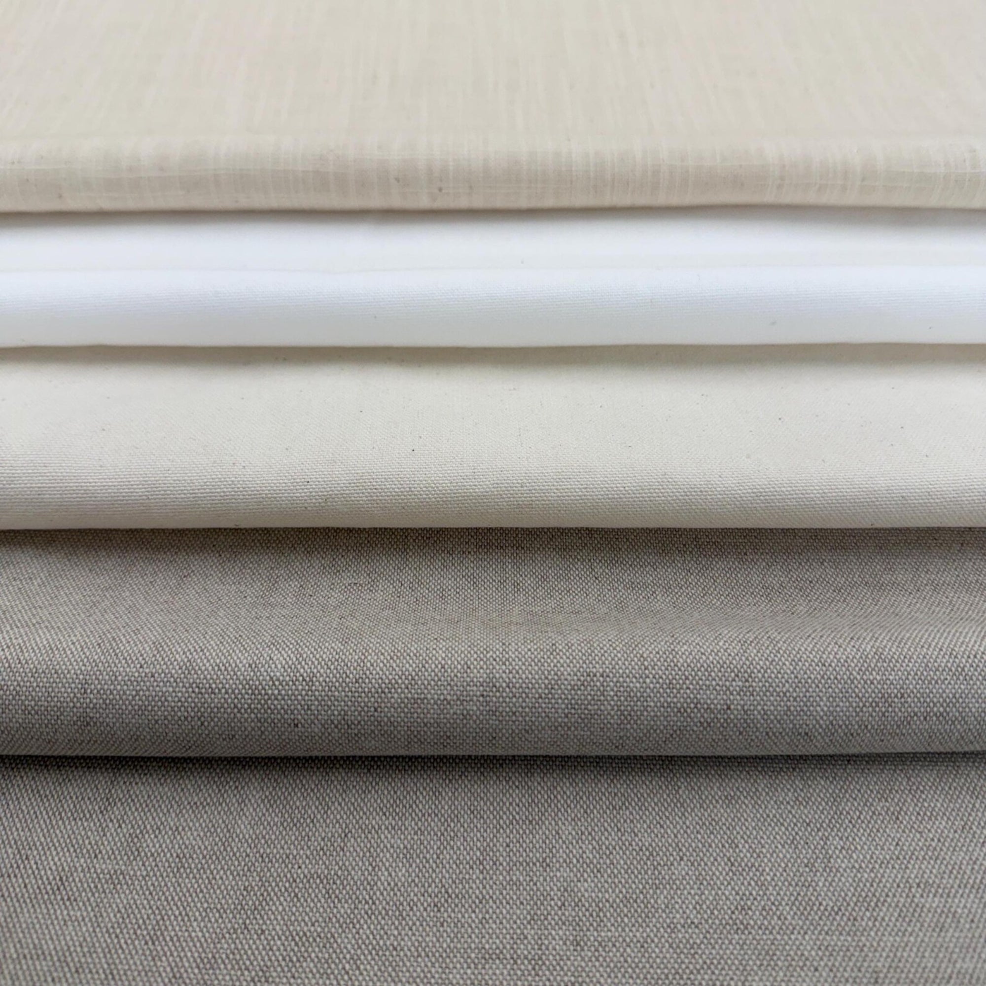 A close-up image of a stack of fabric swatches in various shades of gray and beige.