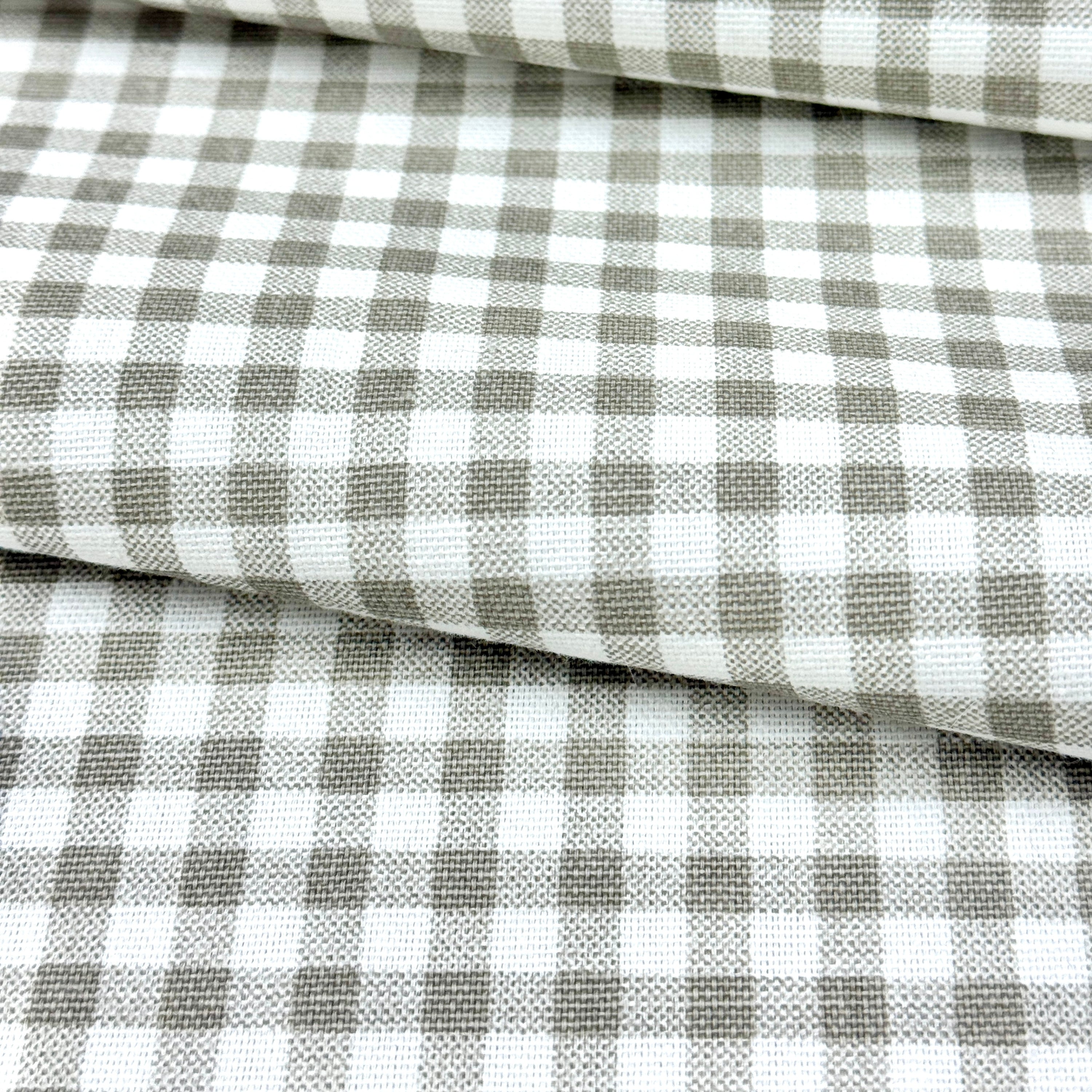 a close-up view of a fabric with a checkered pattern in shades of gray and white. The fabric appears to be folded or rolled, creating a layered effect.