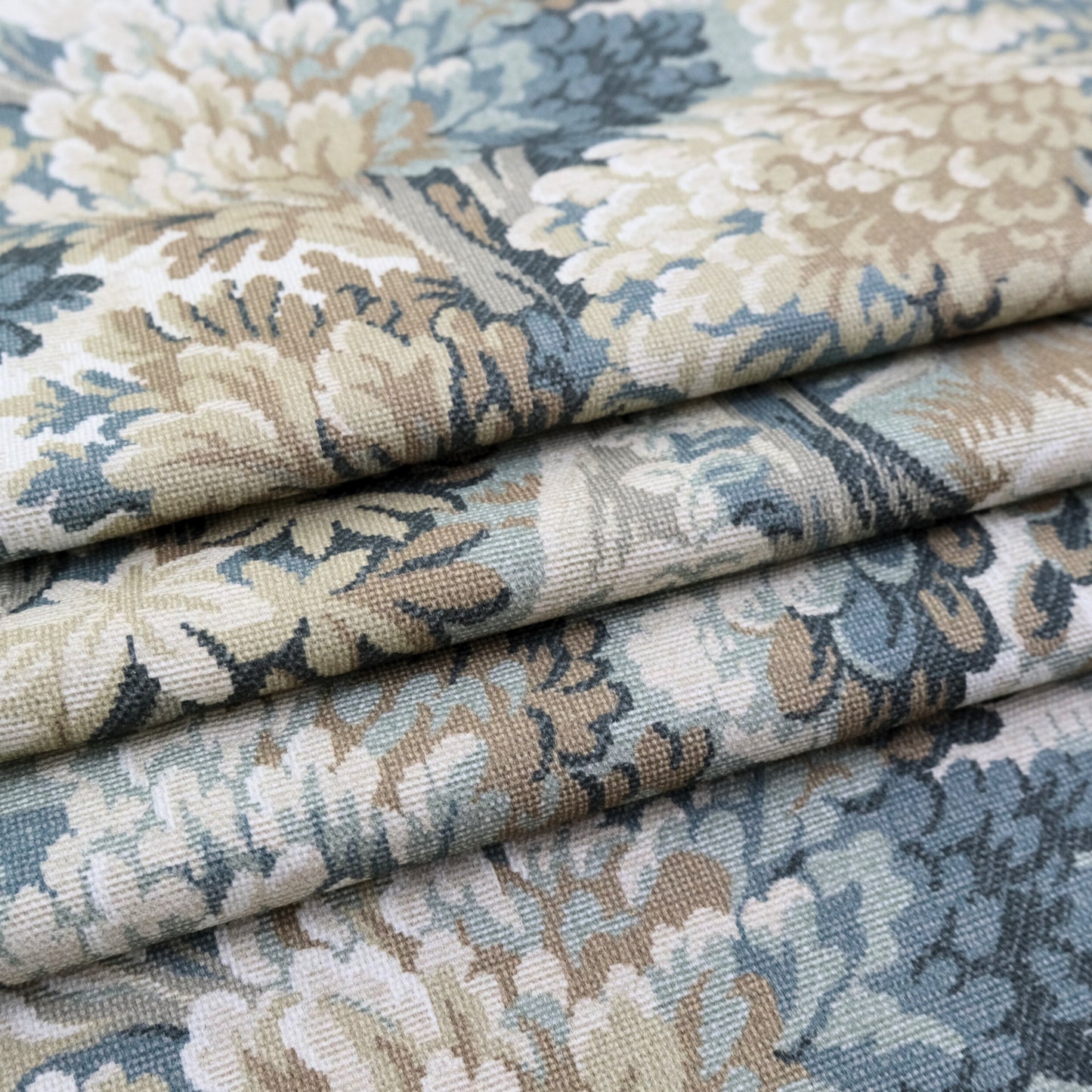 a close-up view of a fabric with a floral pattern in shades of blue, green, and beige. The fabric appears to be folded or rolled, revealing the intricate design and texture of the material.