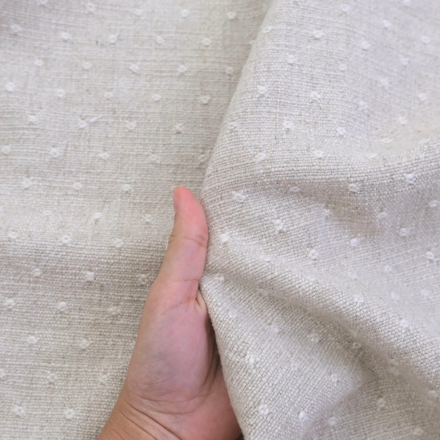 A hand is holding a fabric with small white dots, likely a light-colored material with a textured appearance.
