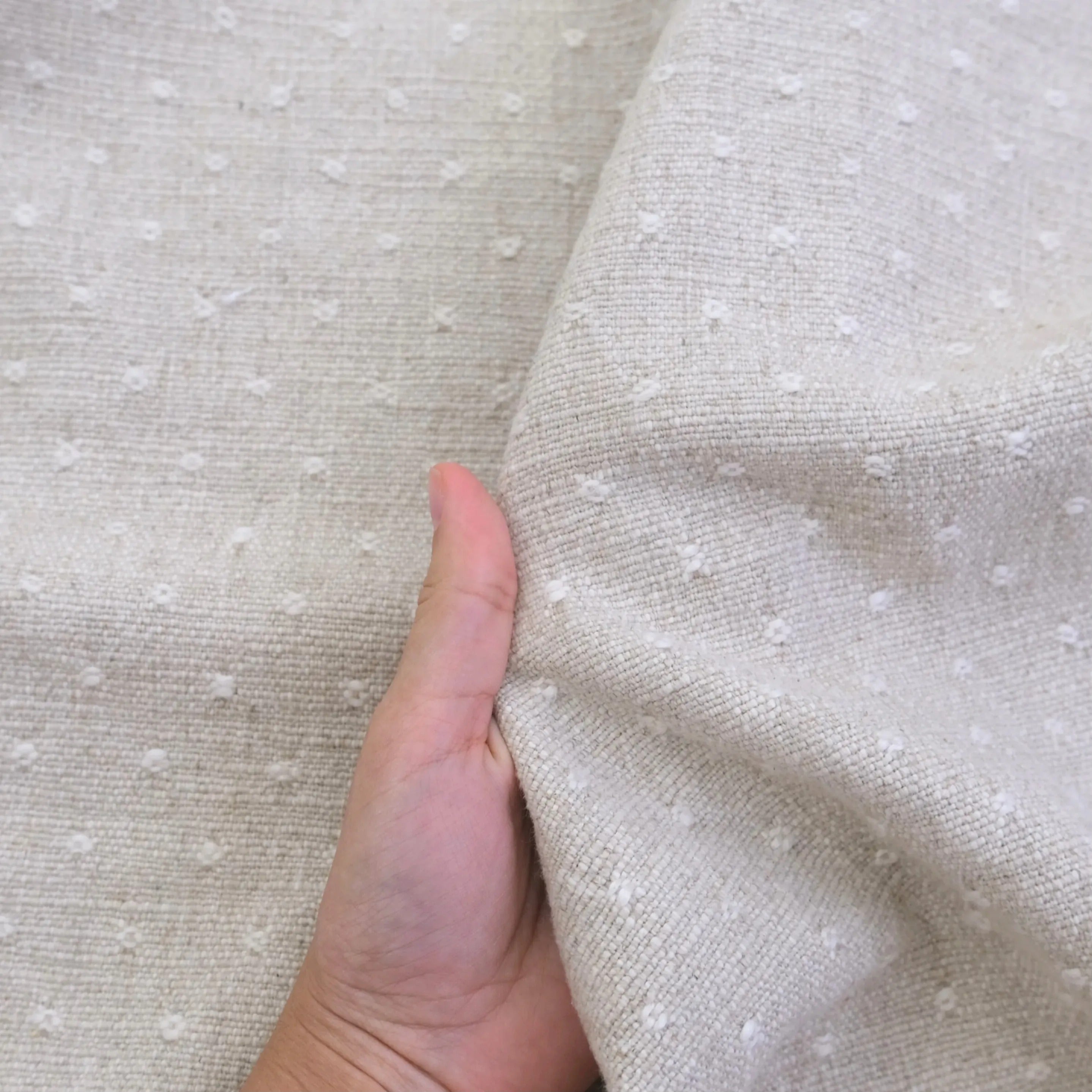 A hand is holding a fabric with small white dots, likely a light-colored material with a textured appearance.