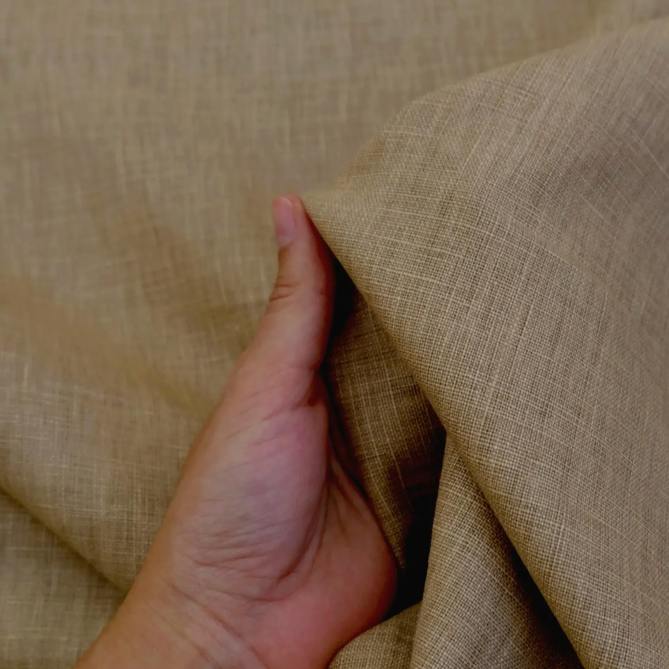 A hand is holding a piece of fabric with a textured, beige-colored appearance.
