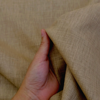 A hand is holding a piece of fabric with a textured, beige-colored appearance.