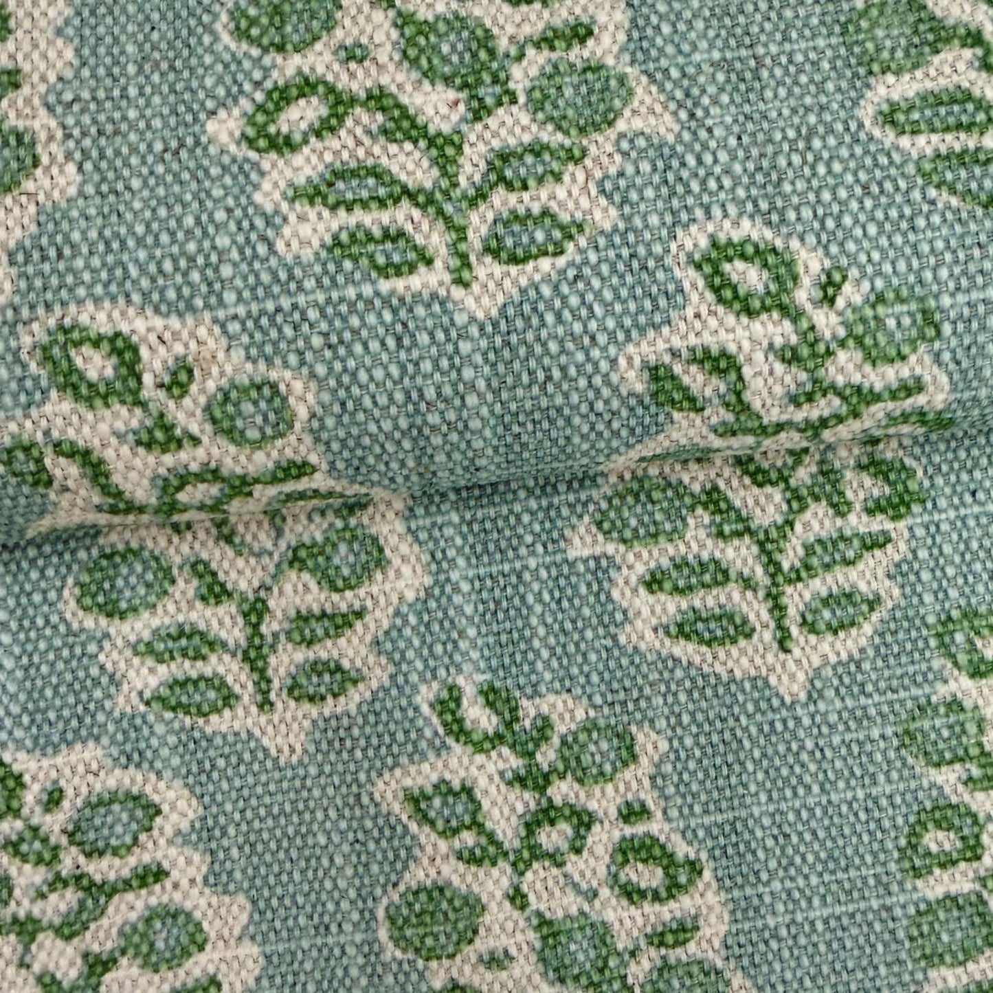 a close-up view of a fabric with a repeating pattern of green and white leaf-like designs.