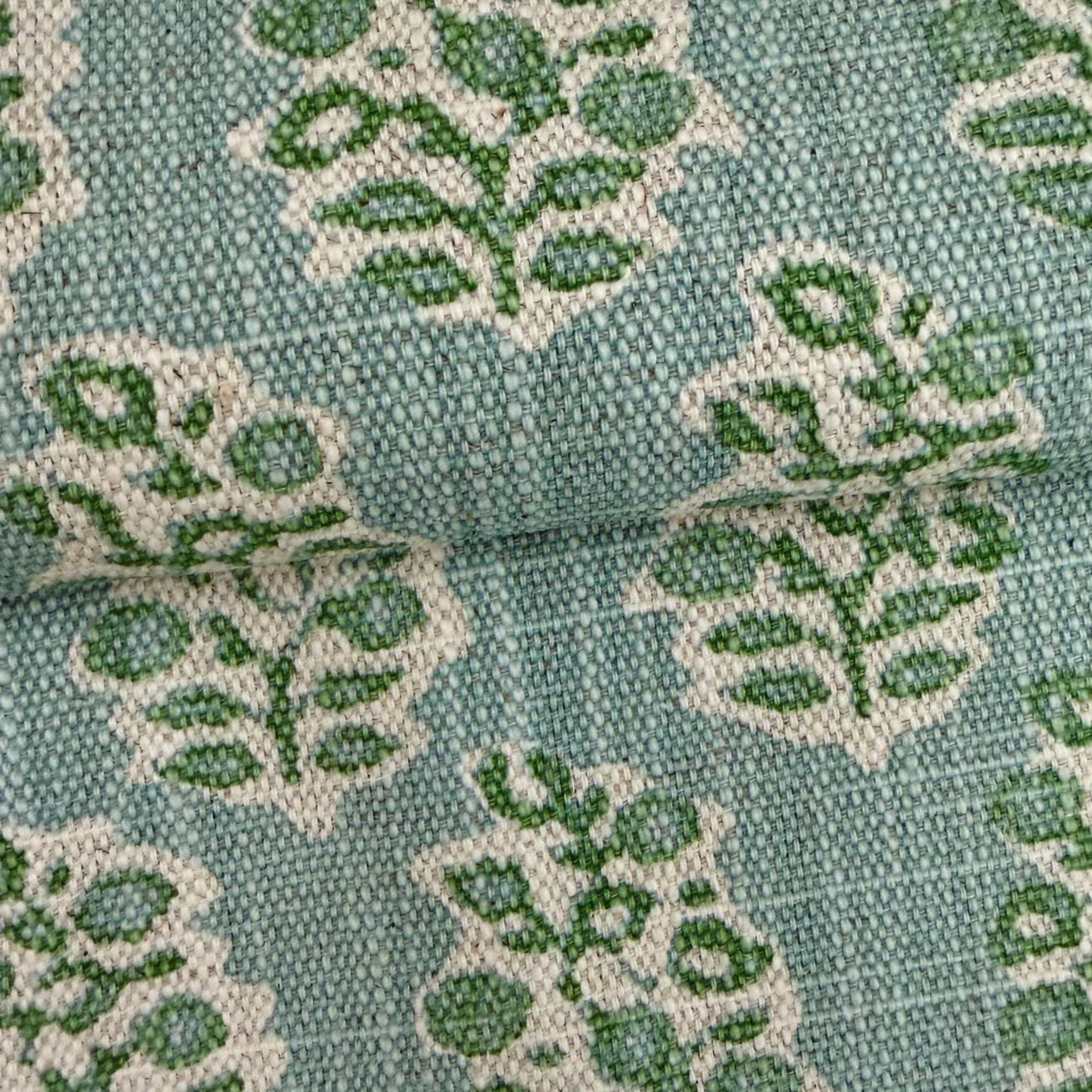 a close-up view of a fabric with a repeating pattern of green and white leaf-like designs.