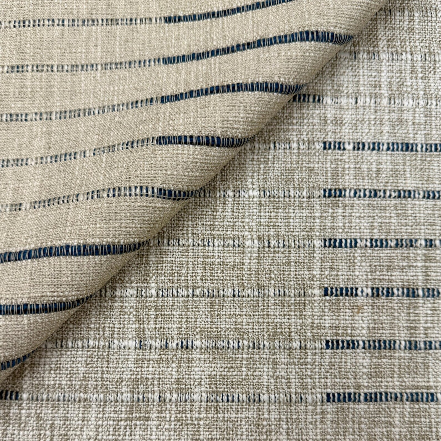 a close-up view of a fabric with a striped pattern in shades of beige and blue. The fabric appears to be made of a woven material, with the stripes running across the entire surface.