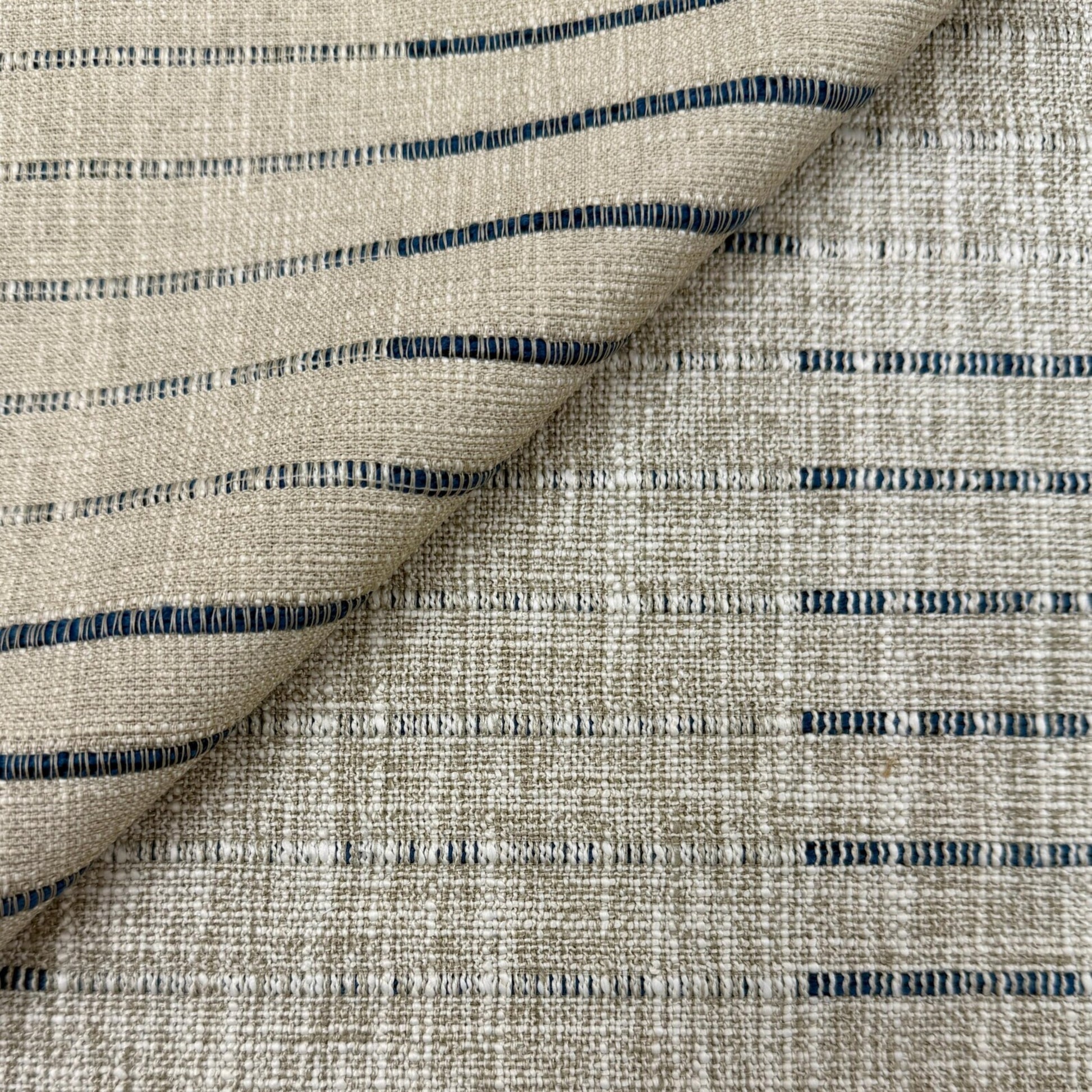 a close-up view of a fabric with a striped pattern in shades of beige and blue. The fabric appears to be made of a woven material, with the stripes running across the entire surface.