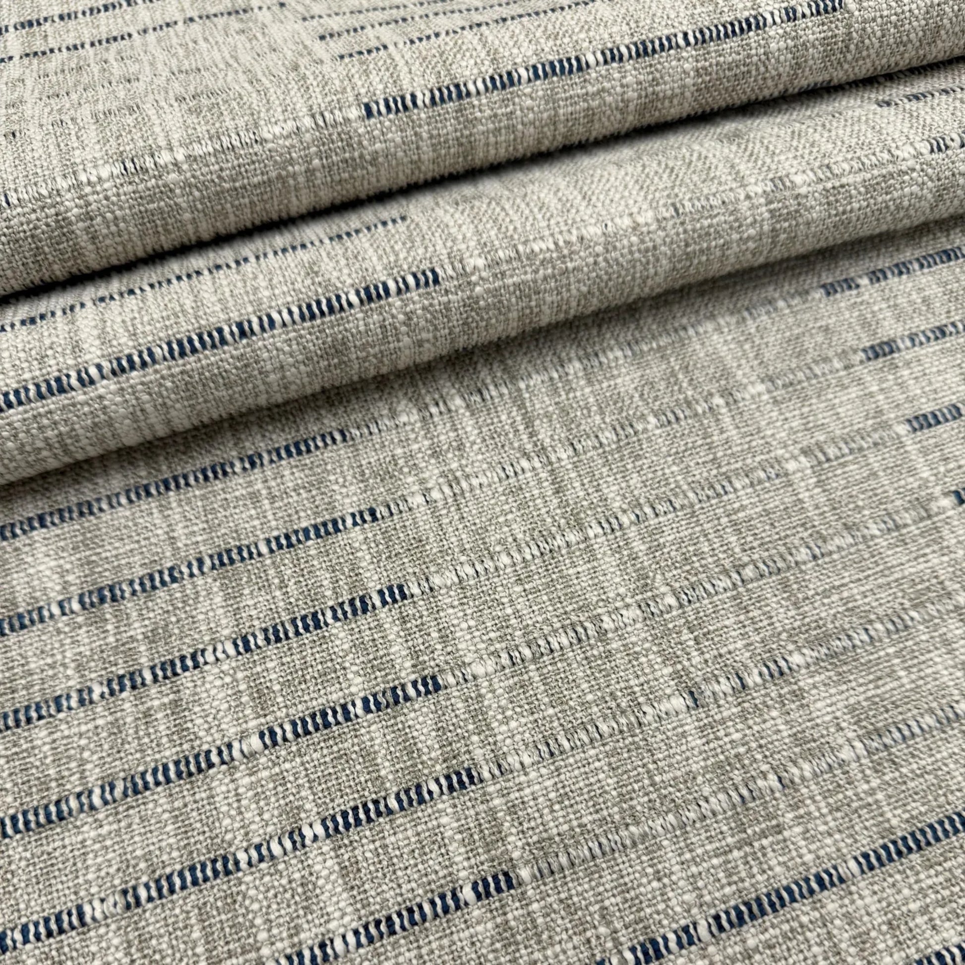 a close-up view of a fabric with a striped pattern in shades of gray and blue. The fabric appears to be folded or rolled, creating a layered effect.