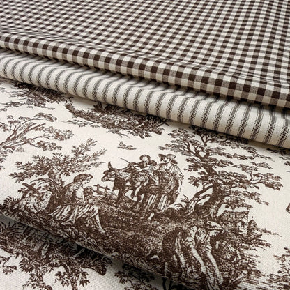 a close-up view of a fabric with a detailed brown and white pattern, including a landscape scene with people and animals. The fabric appears to be a type of quilt or textile with a checkered or gingham-like pattern.