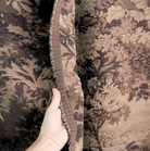 A hand is holding a piece of fabric with a floral pattern, showing the intricate details of the design.