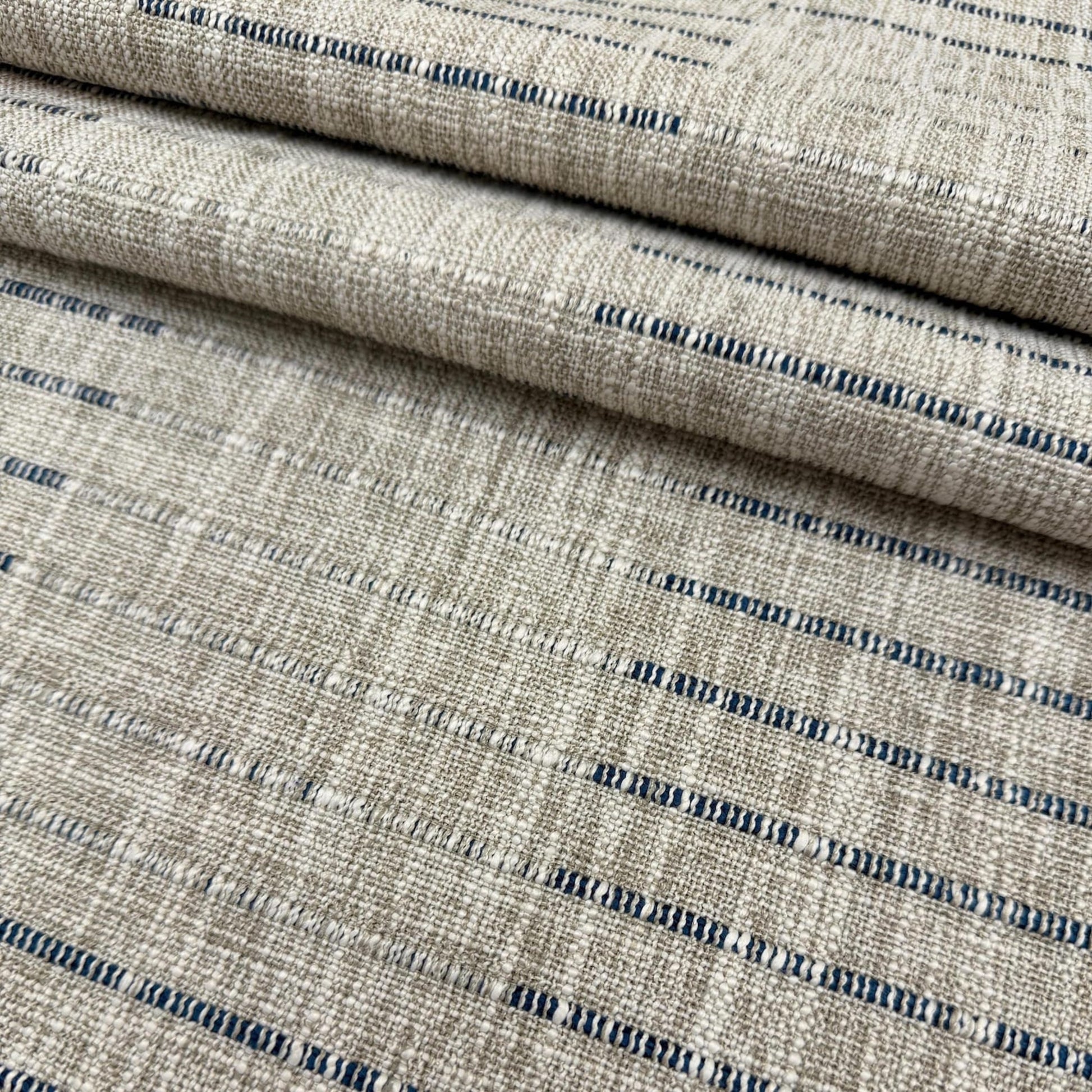 a close-up view of a fabric with a striped pattern in shades of beige and blue. The fabric appears to be folded or rolled, creating a layered effect.