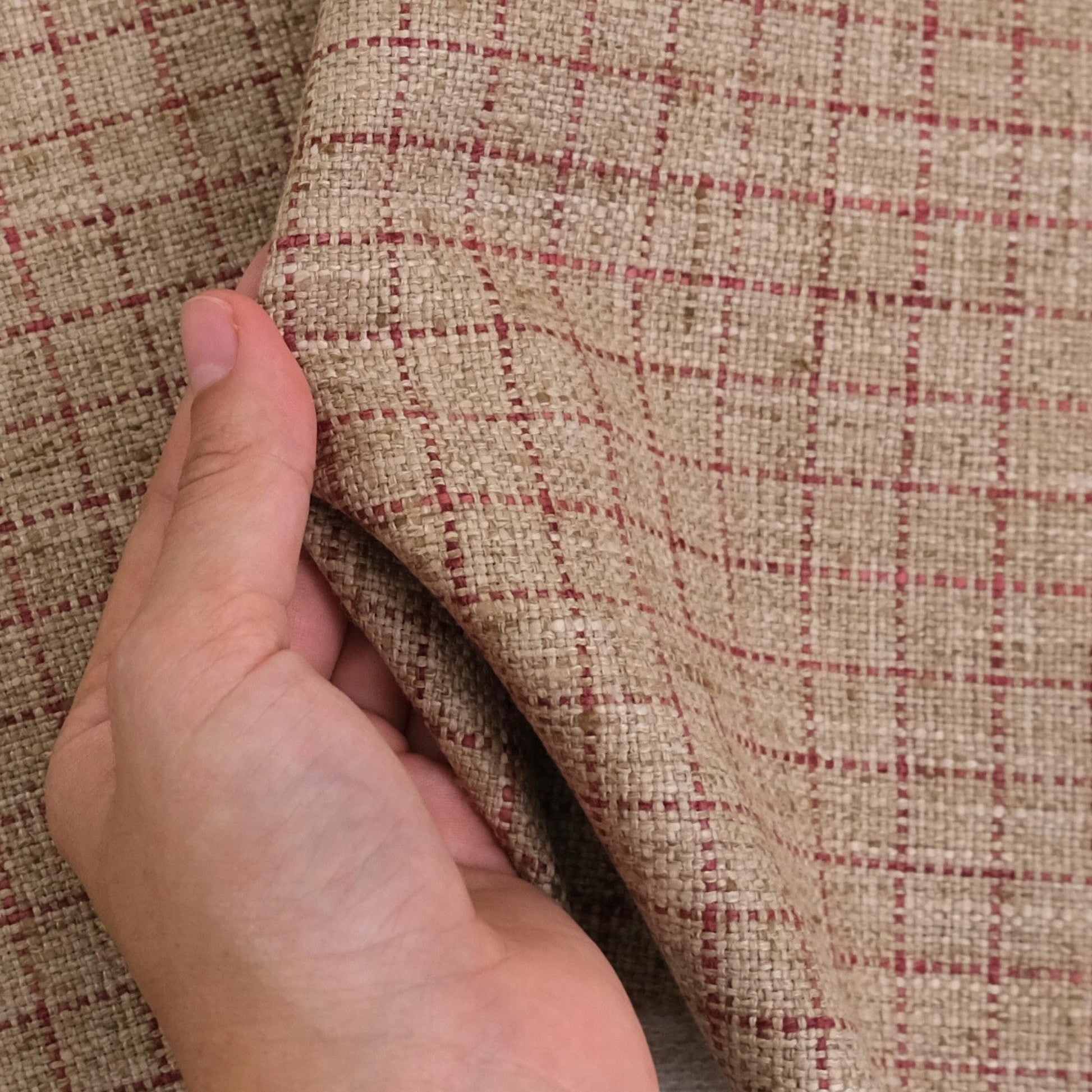 A hand is holding a fabric with a checkered pattern in red and beige colors.