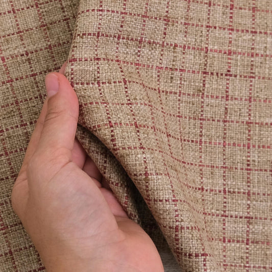 A hand is holding a fabric with a checkered pattern in red and beige colors.