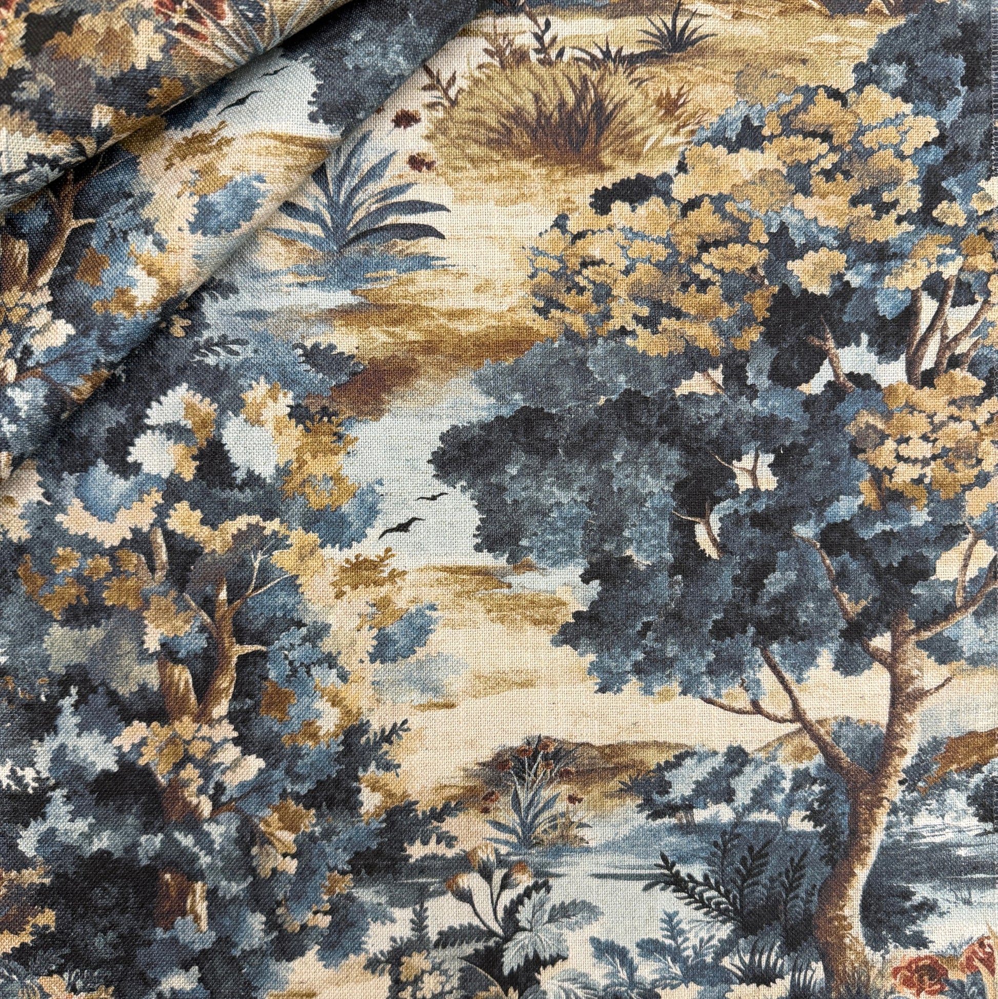 a close-up view of a fabric with a detailed, colorful pattern of trees, bushes, and other natural elements. The fabric appears to be a textile or wallpaper with a landscape design, possibly used for decorative purposes or as a home textile.