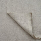 a close-up view of a piece of fabric with a textured, woven appearance. The fabric appears to be made of a light-colored material, possibly linen or a similar type of textile. The fabric is folded over itself, creating a sense of depth and dimension in the image.