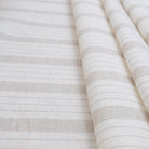 Taupe stripe linen fabric folded to showcase its soft airy weave and subtle neutral stripe design. This lightweight material is ideal for sewing curtains, table linens, pillow covers, and cottagecore-inspired home décor. Perfect for DIY sewing projects, rustic farmhouse accents, neutral minimalist interiors, and versatile décor crafts where natural linen texture adds charm and durability.